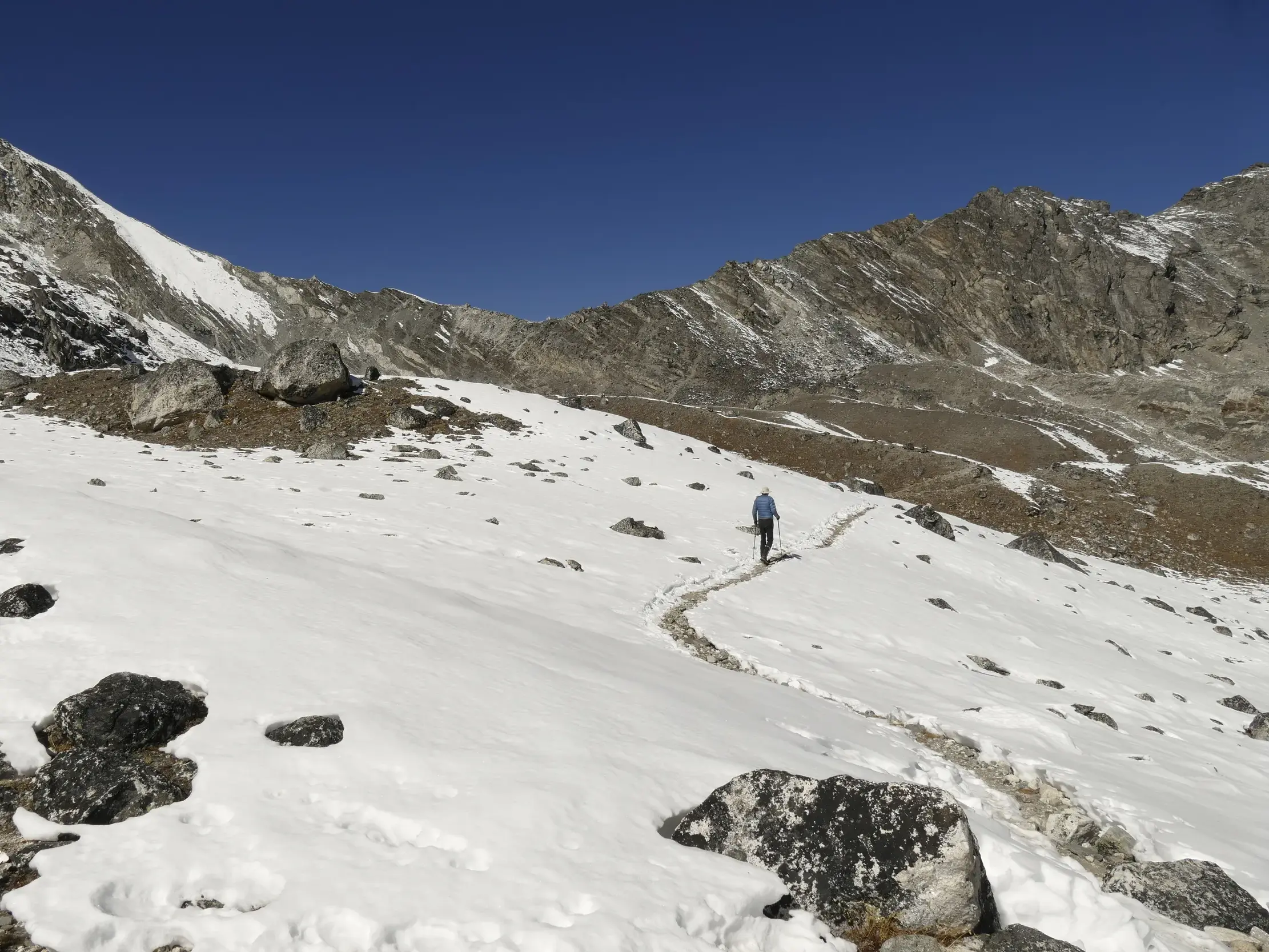 Ein Trekker folgt einem schmalen Pfad durch eine verschneite Hochgebirgslandschaft auf dem Weg zu einem Pass im Himalaya Nepals.