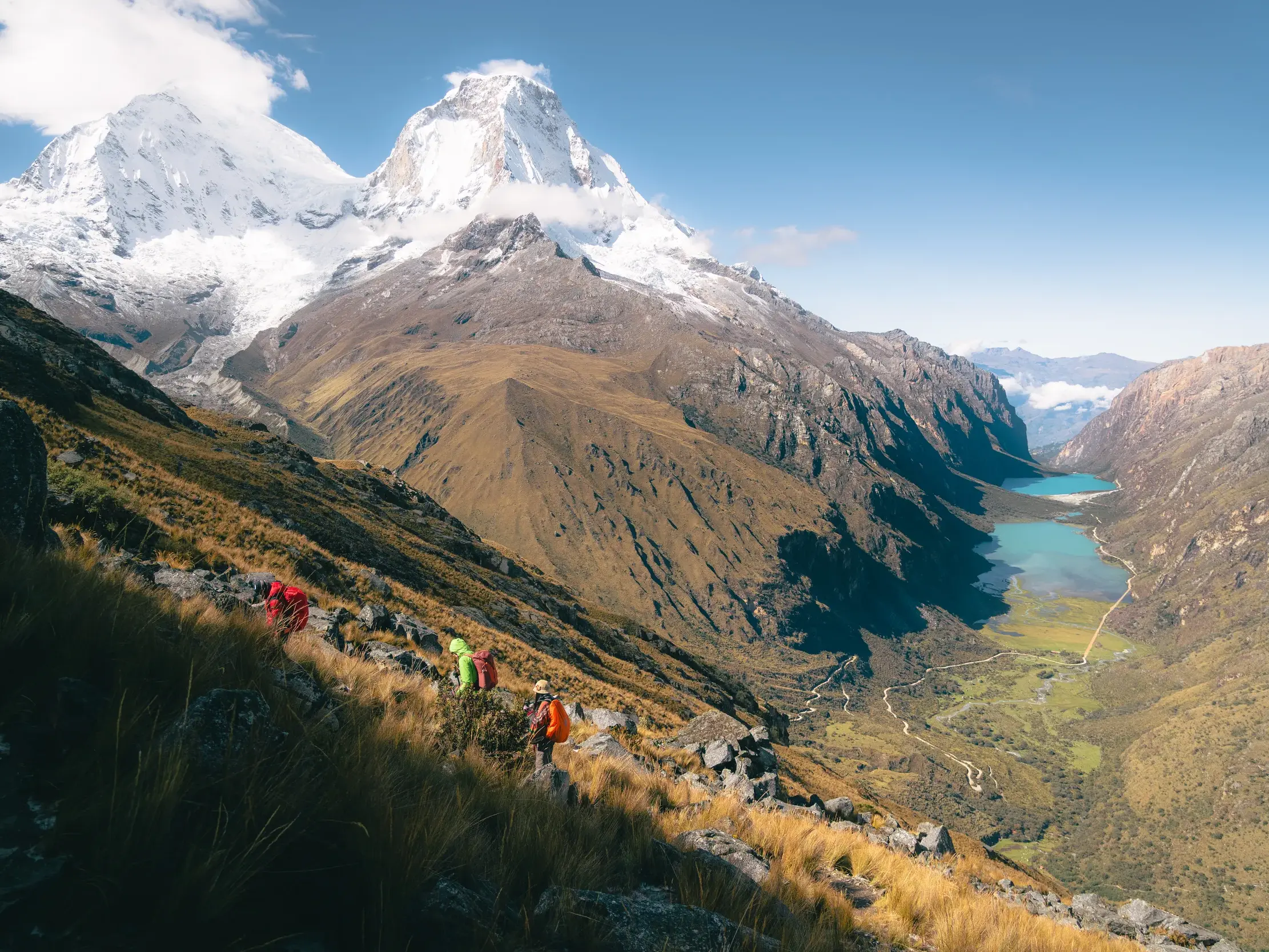 Eine Wandergruppe auf einem Bergpfad in der Cordillera Blanca mit Blick auf schneebedeckte Gipfel und türkise Bergseen im Tal.