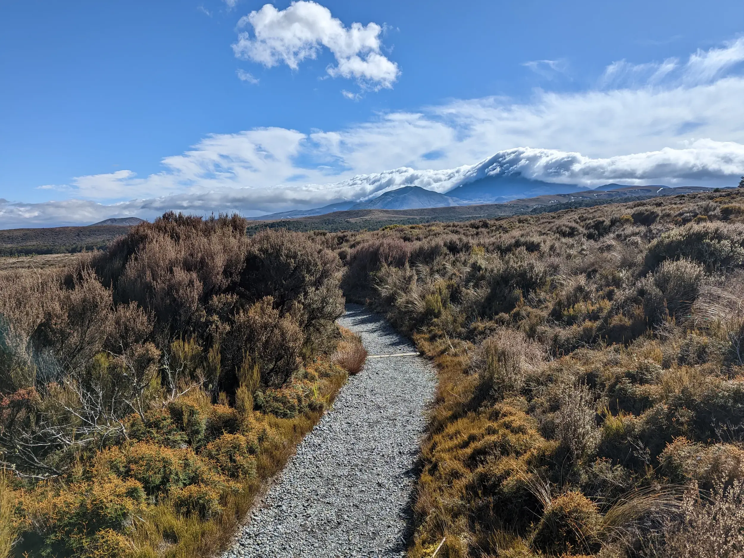 Ein Schotter-Wanderweg führt durch die weite Vulkanlandschaft des Tongariro Nationalparks zum wolkenbedeckten Mount Ruapehu.