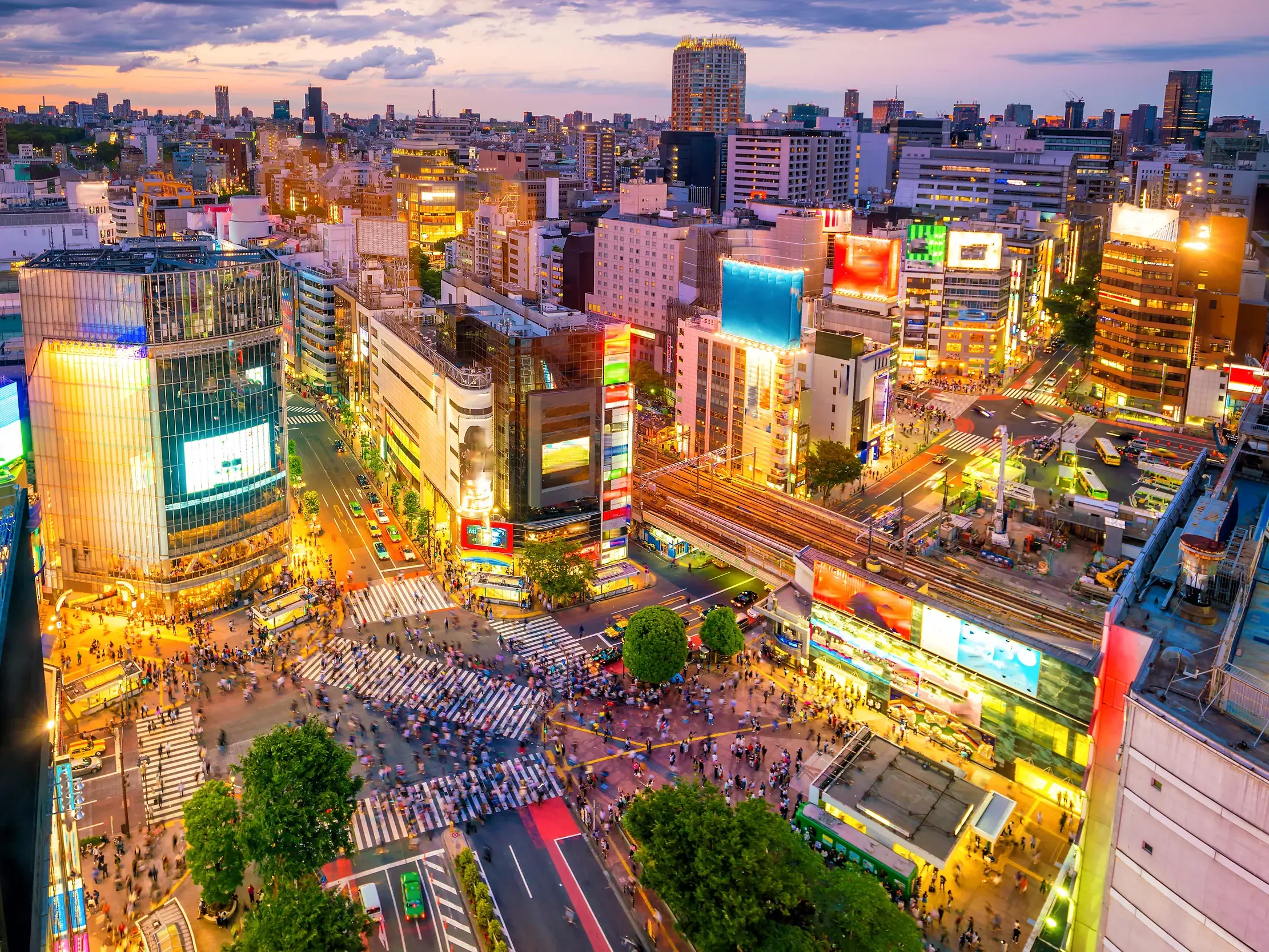 Menschenmassen überqueren die berühmte Shibuya-Kreuzung in Tokio bei Dämmerung, umgeben von hell leuchtenden Neonreklamen.
