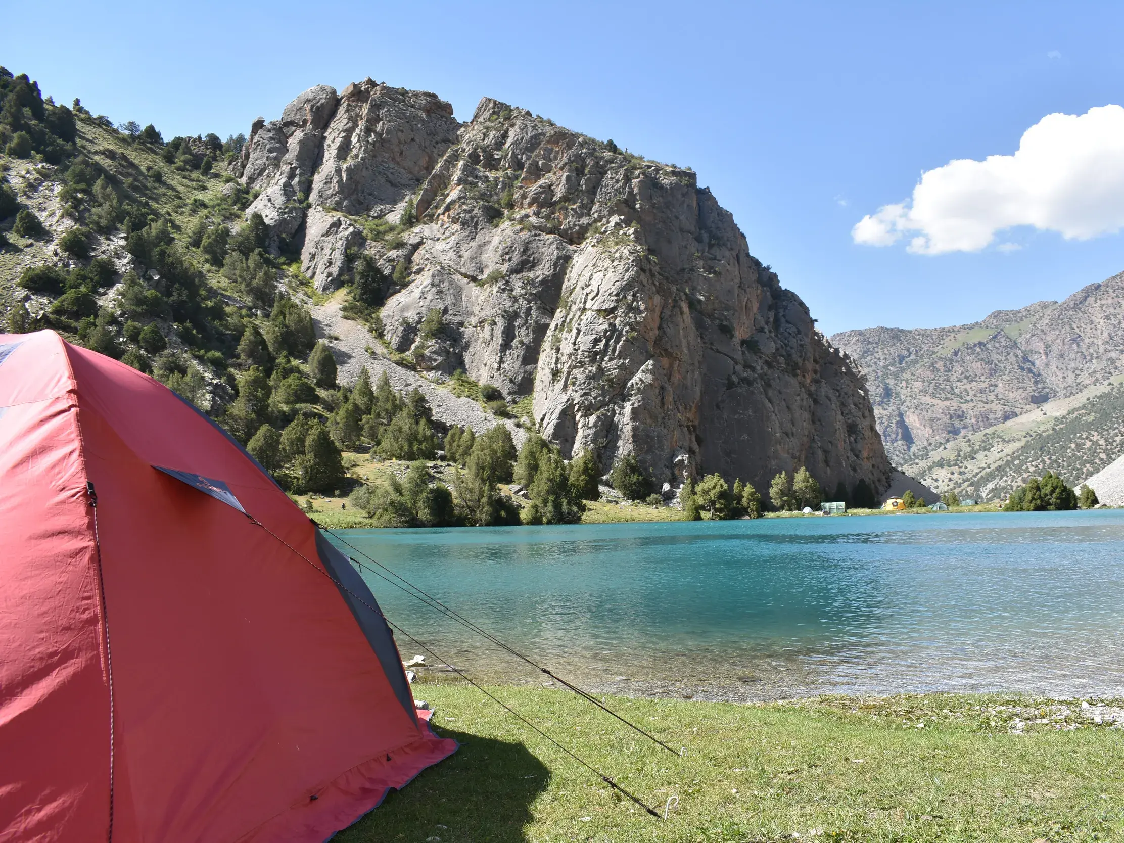 Rotes Zelt am Ufer des türkisen Alaudin-Sees beim Trekking im Fan-Gebirge in der Bergwelt von Tadschikistan.