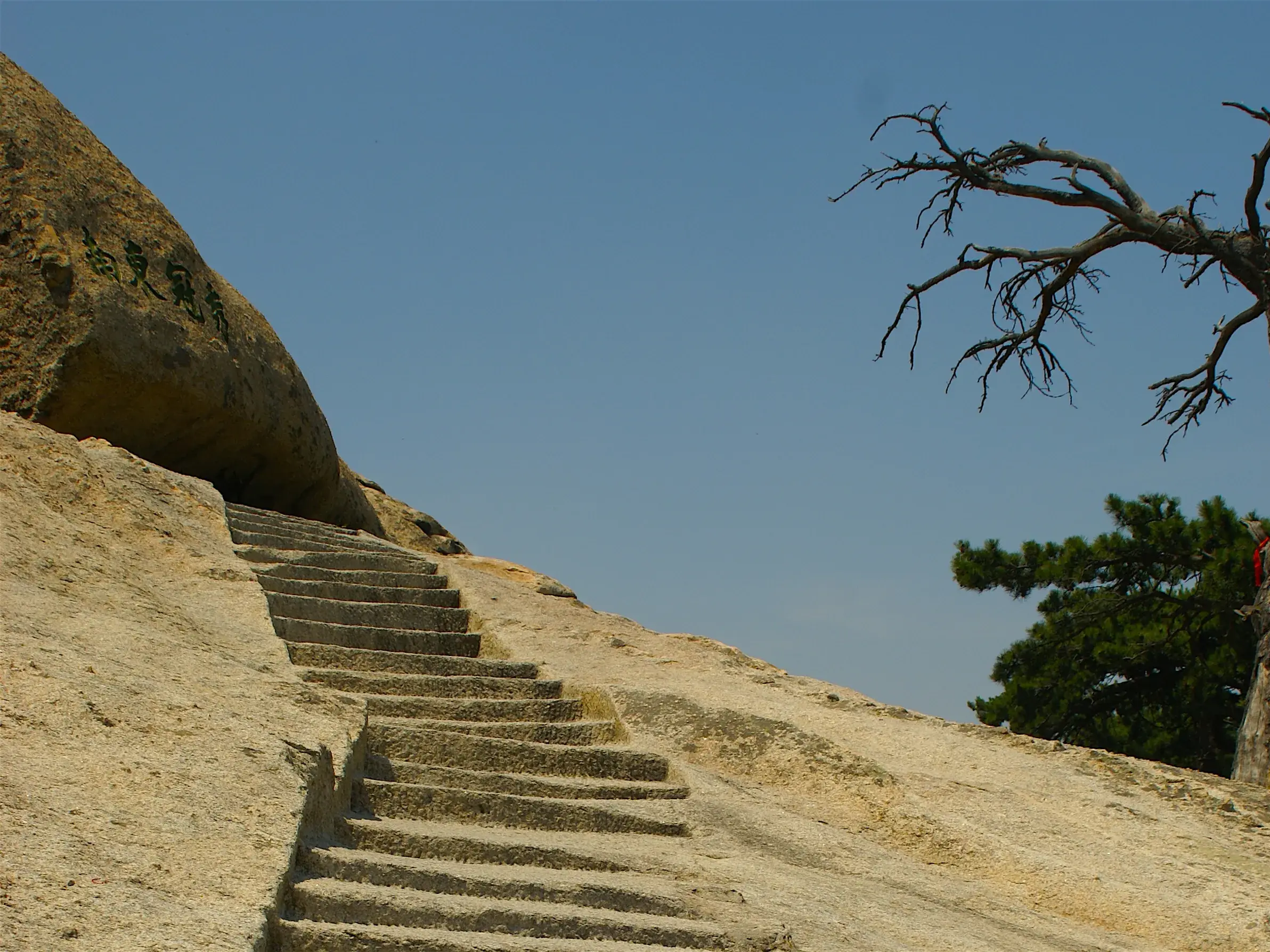 Steile, in den Felsen gehauene Treppe auf dem Wanderweg am heiligen Berg Hua Shan in China unter klarem, blauem Himmel.