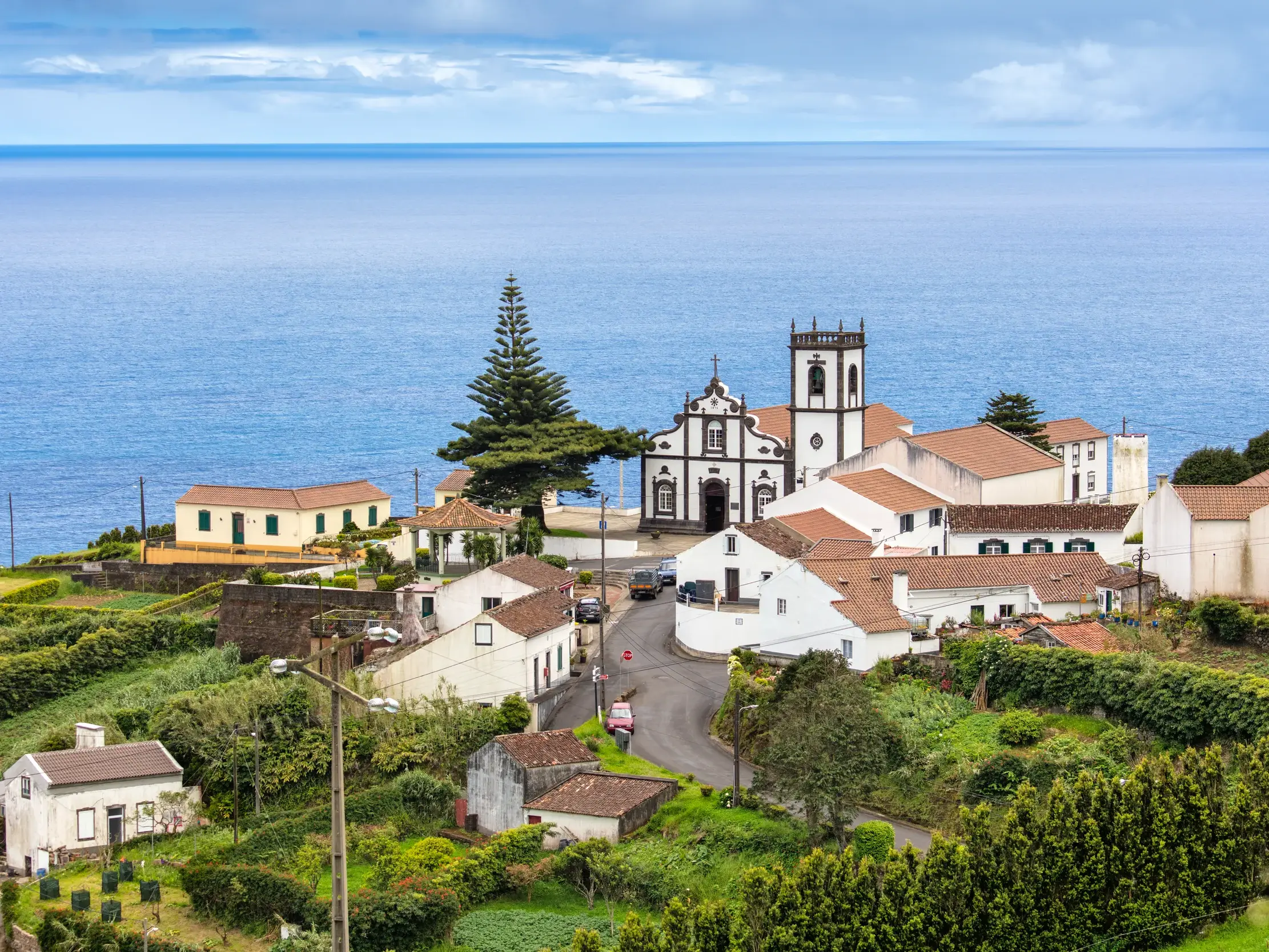 Das Küstendorf Lajes do Pico auf der Azoreninsel Pico mit seiner markanten Kirche, umgeben von grünen Hügeln am Atlantik.