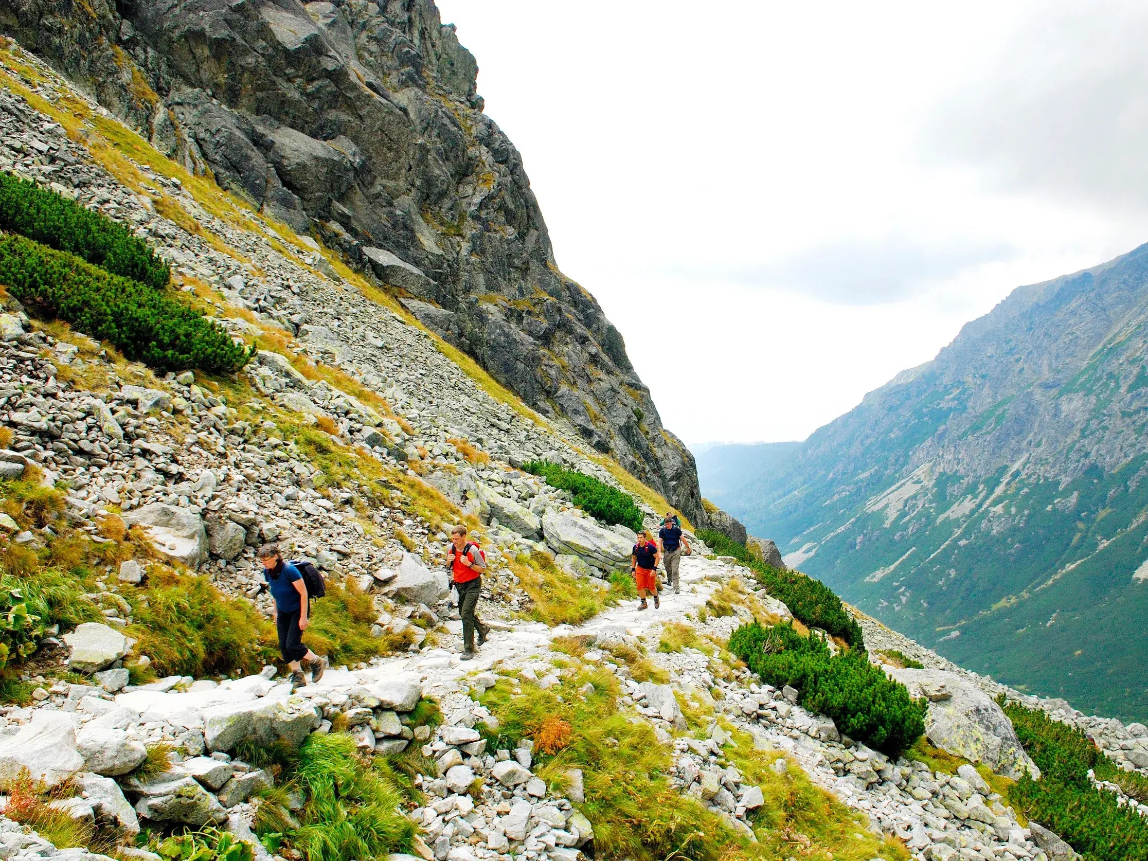 Eine Wandergruppe auf einem schmalen Felsensteig mit weitem Blick in ein grünes Tal im Nationalpark Hohe Tatra.