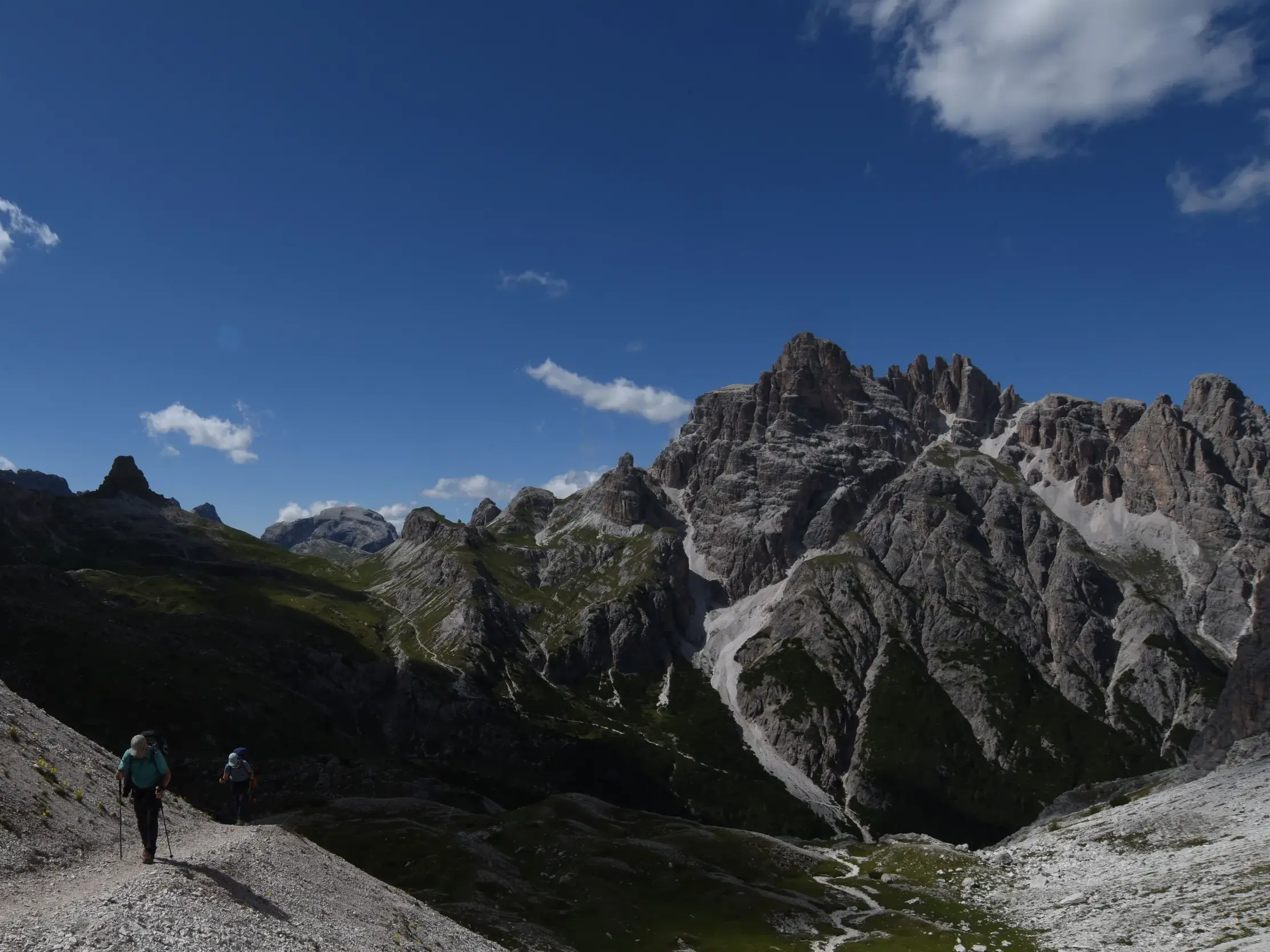 Zwei Wanderer auf einem schmalen Geröllpfad während einer Hüttenwanderung mit Blick auf die Felsgipfel der Sextener Dolomiten.