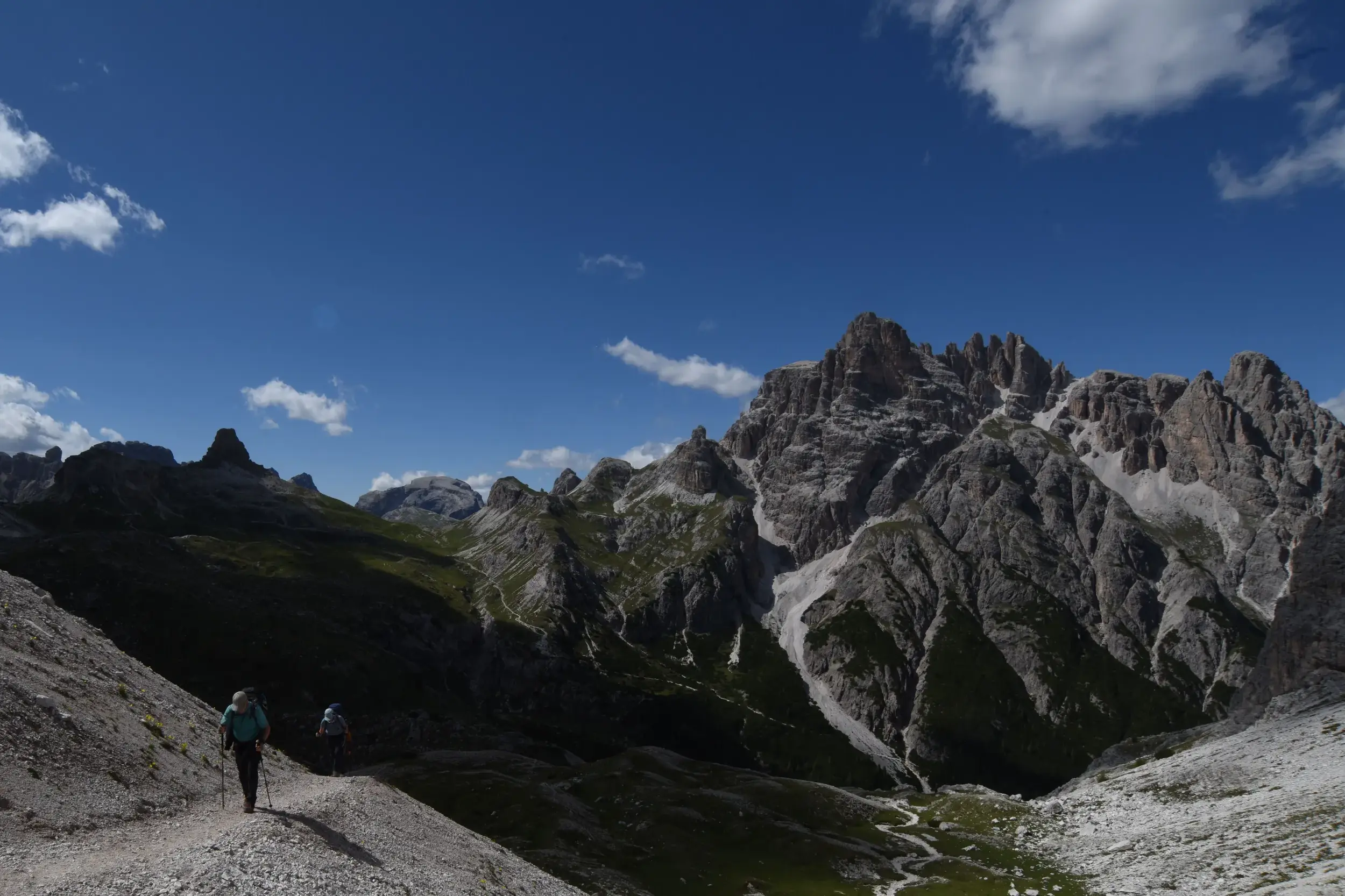 Zwei Wanderer auf einem schmalen Geröllpfad während einer Hüttenwanderung mit Blick auf die Felsgipfel der Sextener Dolomiten.