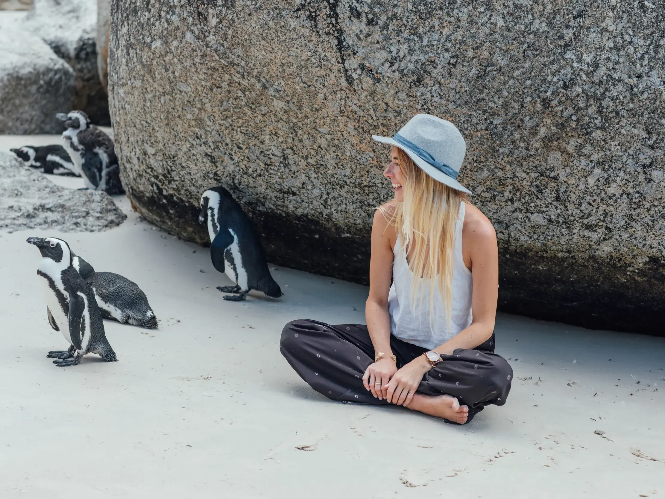 Eine junge Reisende beobachtet bei einer Kleingruppenreise am Boulders Beach in Südafrika neugierig Brillenpinguine.