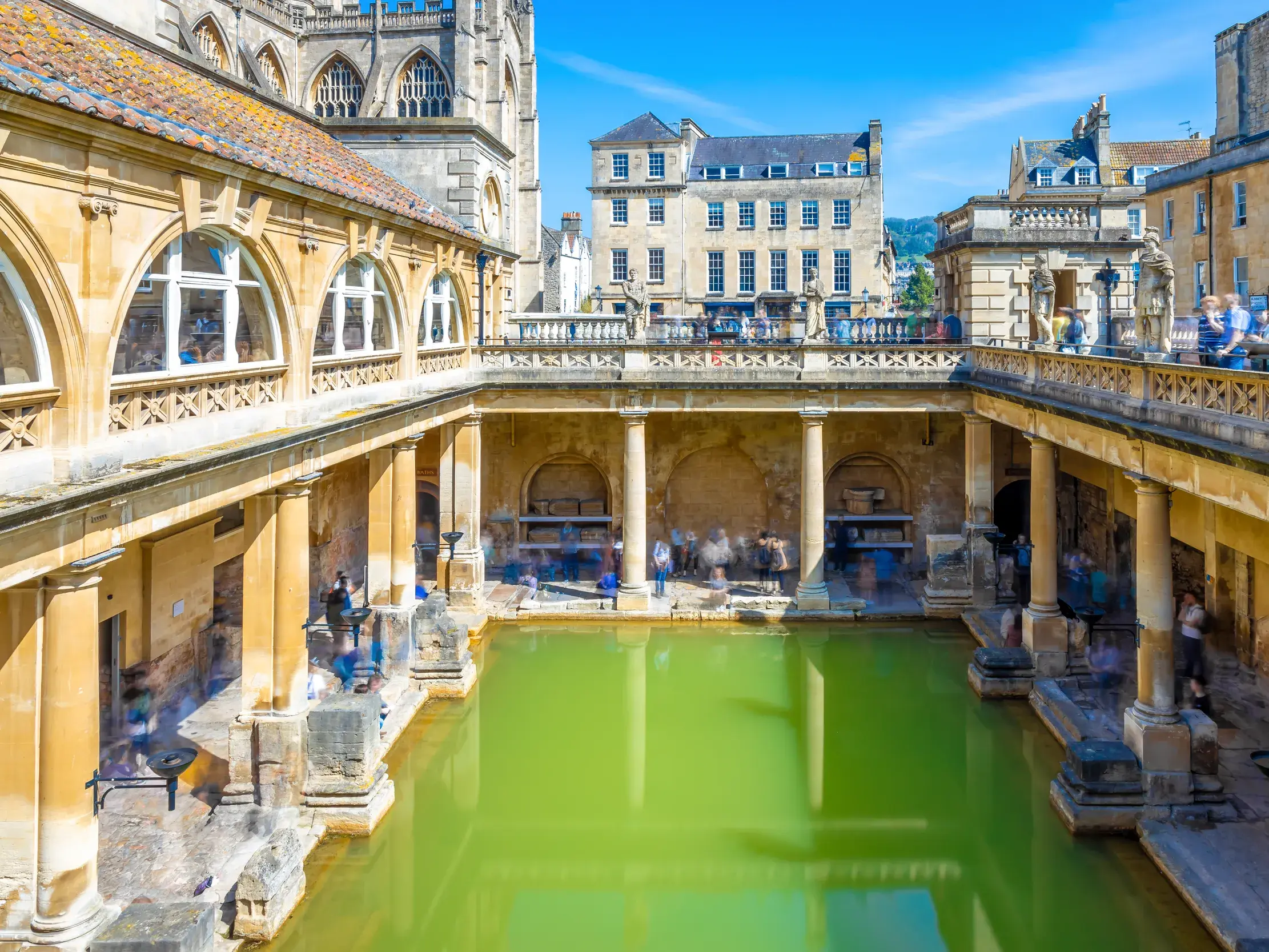 Historische Römische Bäder in Bath mit dem grünen Wasser des Großen Bades, umgeben von antiken Säulengängen bei Sonnenschein.