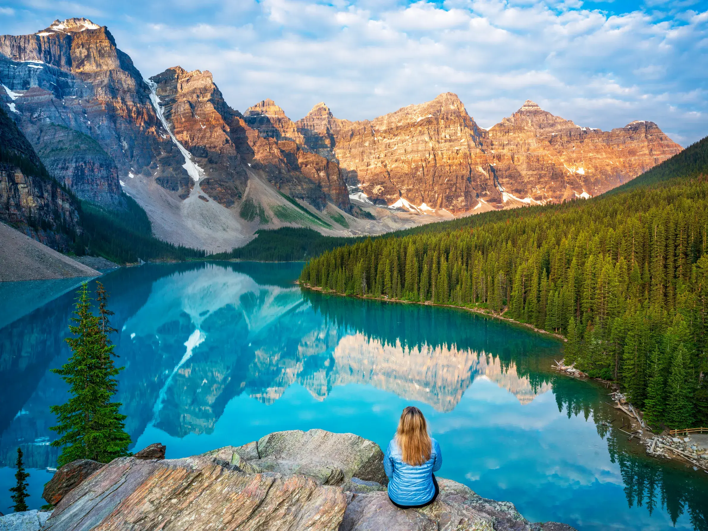 Teilnehmerin einer Studienreise blickt auf den türkisen Moraine Lake im Banff-Nationalpark, dessen Gipfel sich im Wasser spiegeln.