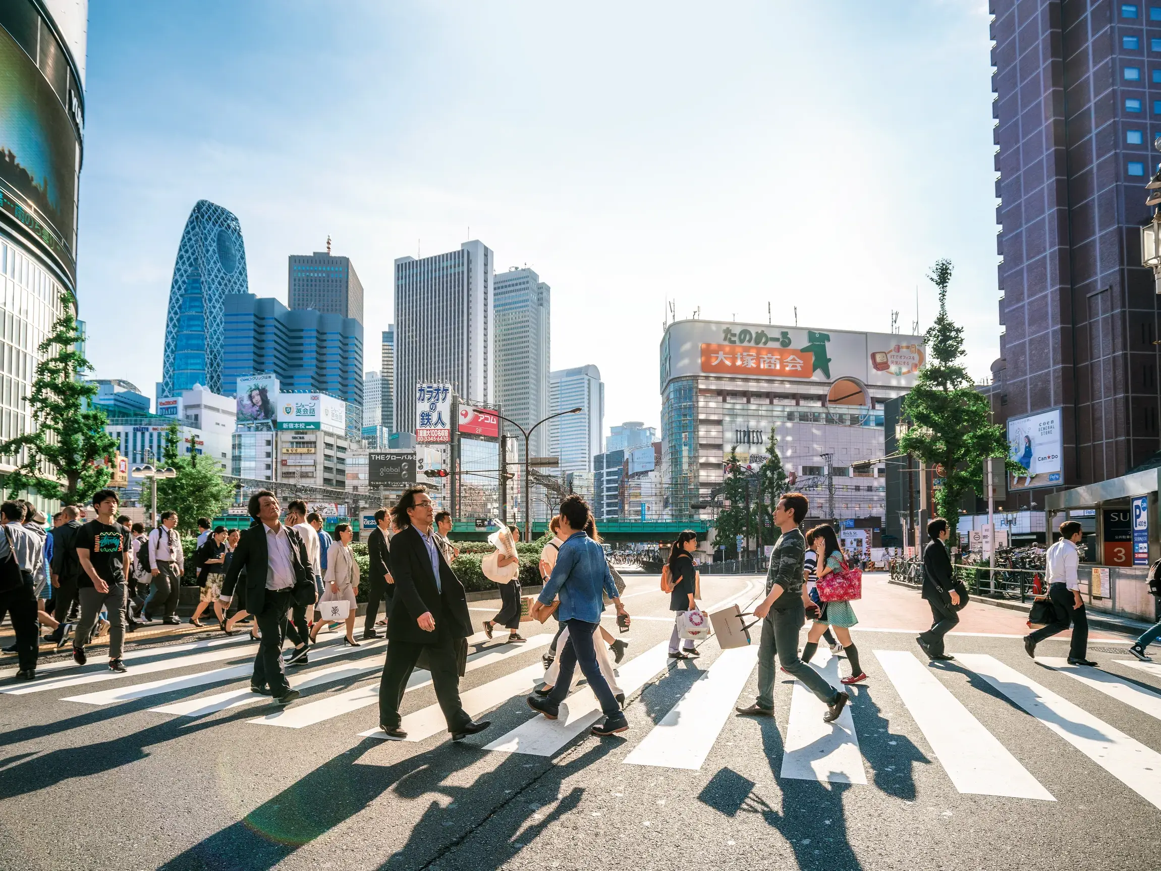 Fußgänger überqueren einen Zebrastreifen im Stadtteil Shinjuku in Tokio vor der Skyline mit dem markanten Cocoon Tower.