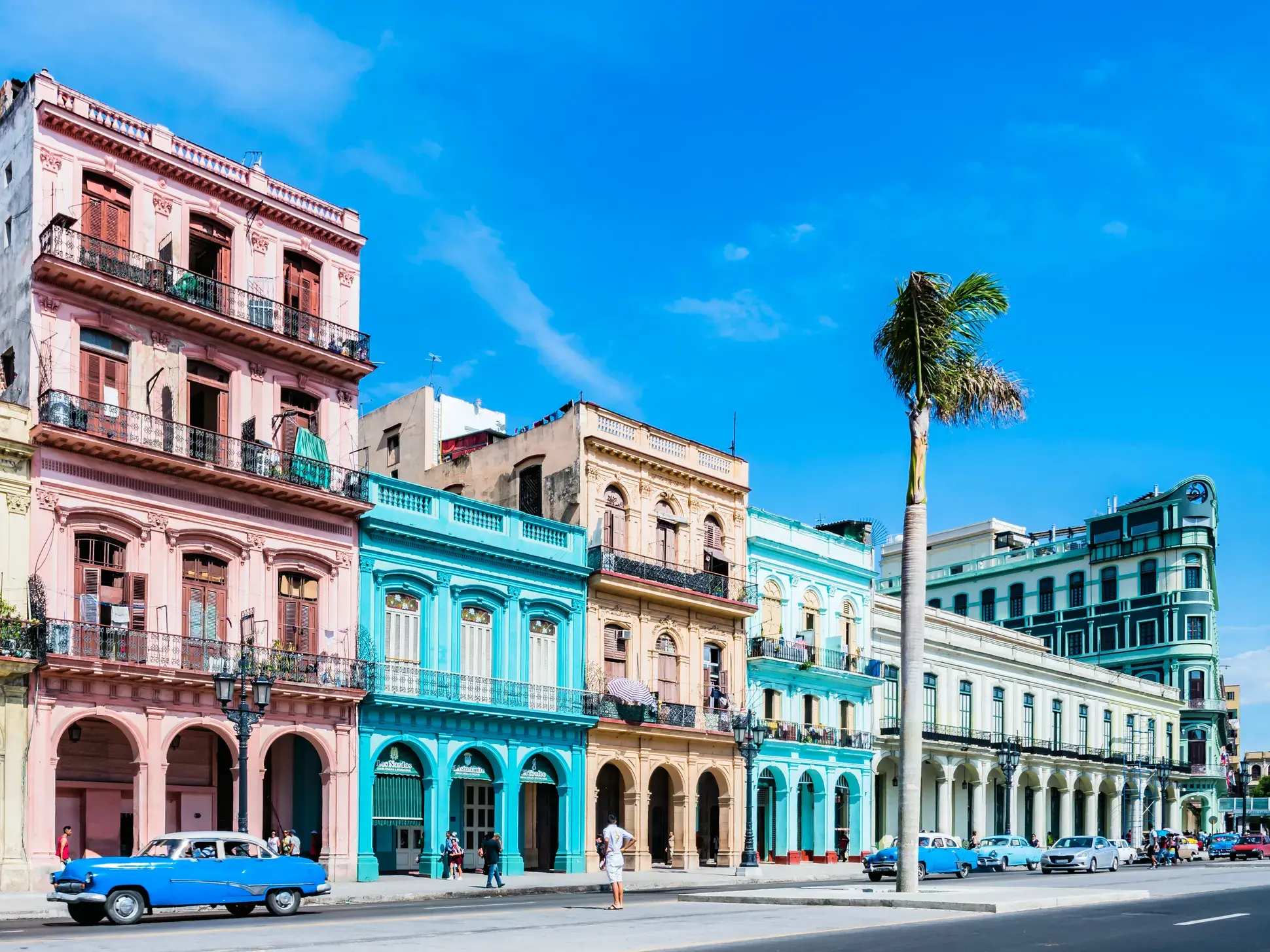 Blauer amerikanischer Oldtimer an einer Straße vor bunten Kolonialfassaden in der Altstadt von Havanna an einem sonnigen Tag.