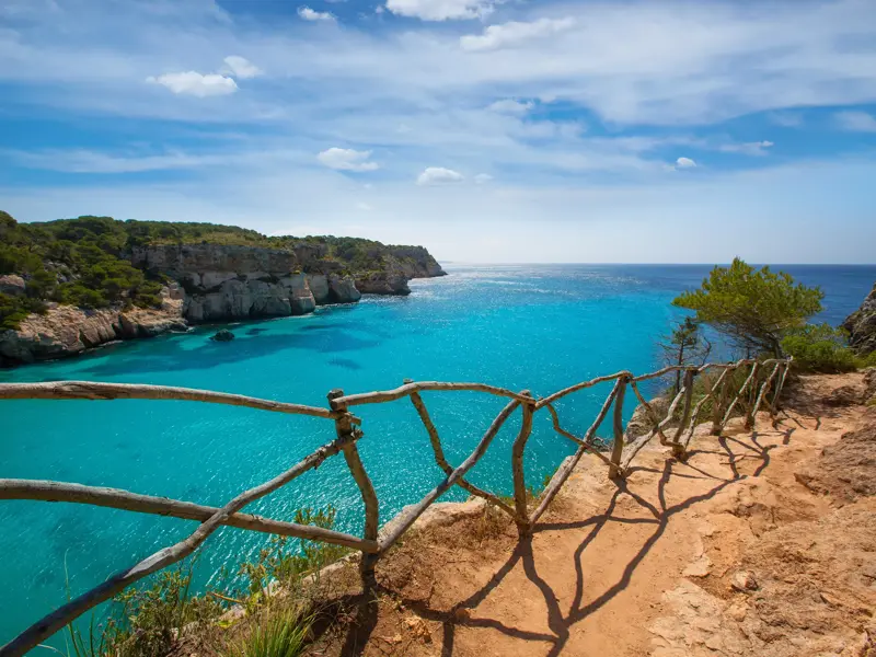 Blick vom Wanderweg Camí de Cavalls über die Felsküste auf die türkisfarbene Bucht Cala Macarella auf der Insel Menorca.