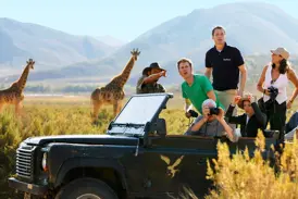 Ein Studiosus-Reiseleiter zeigt seiner Gruppe auf einer Studienreise im Jeep zwei Giraffen in der Savanne Südafrikas.