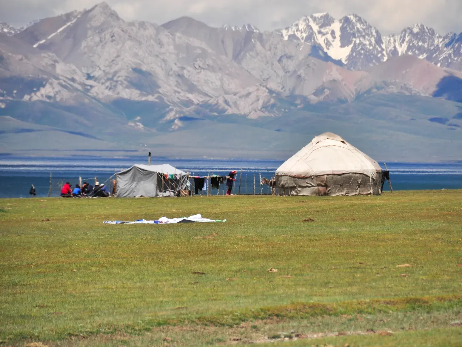 Jurtencamp von Nomaden am blauen Songköl See in Kirgistan, im Hintergrund die hohen Gipfel des Tian-Shan-Gebirges.