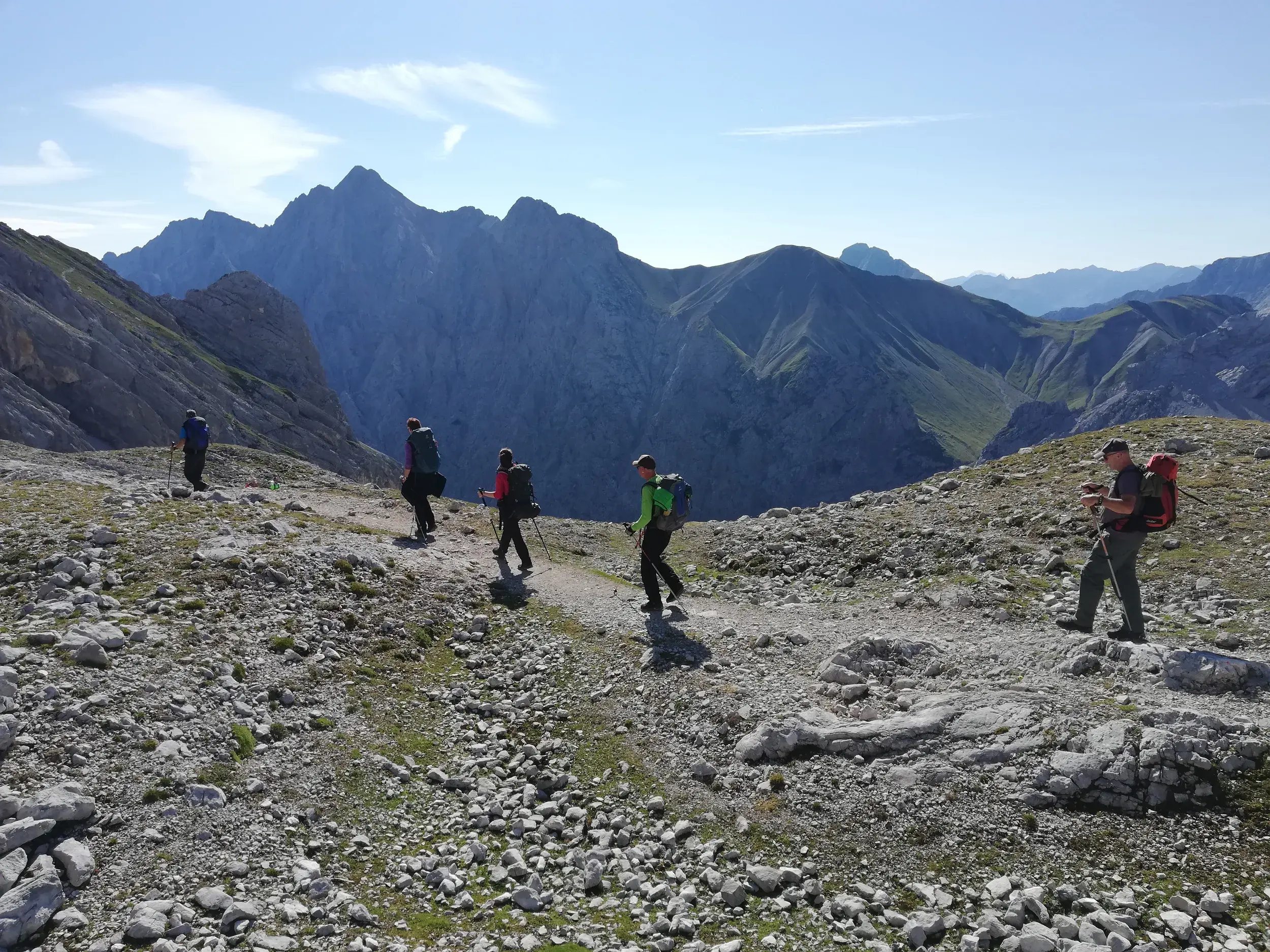 Eine kleine Wandergruppe bei der Alpenüberquerung auf einem kargen Gebirgspfad mit Blick auf die Gipfel der Stubaier Alpen.