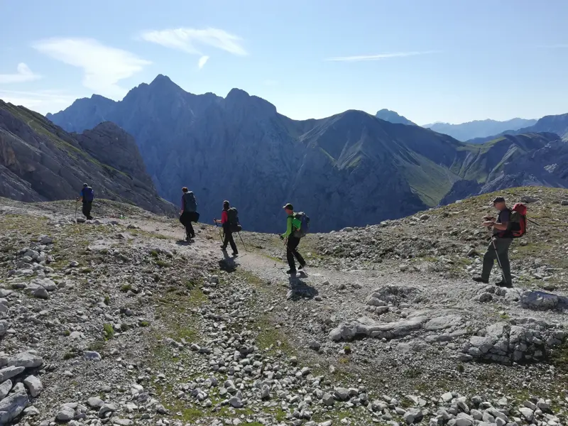 Eine kleine Wandergruppe bei der Alpenüberquerung auf einem kargen Gebirgspfad mit Blick auf die Gipfel der Stubaier Alpen.