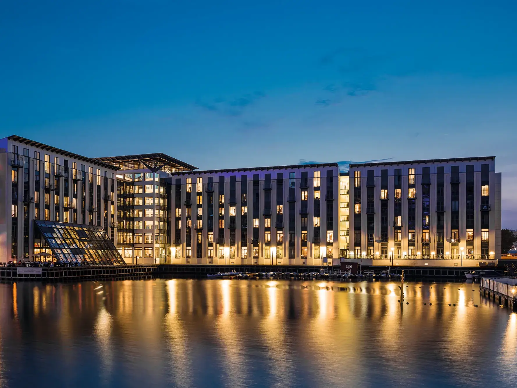 Das moderne Hotel Copenhagen Island in der Abenddämmerung, dessen Lichter sich malerisch im Hafenbecken spiegeln.