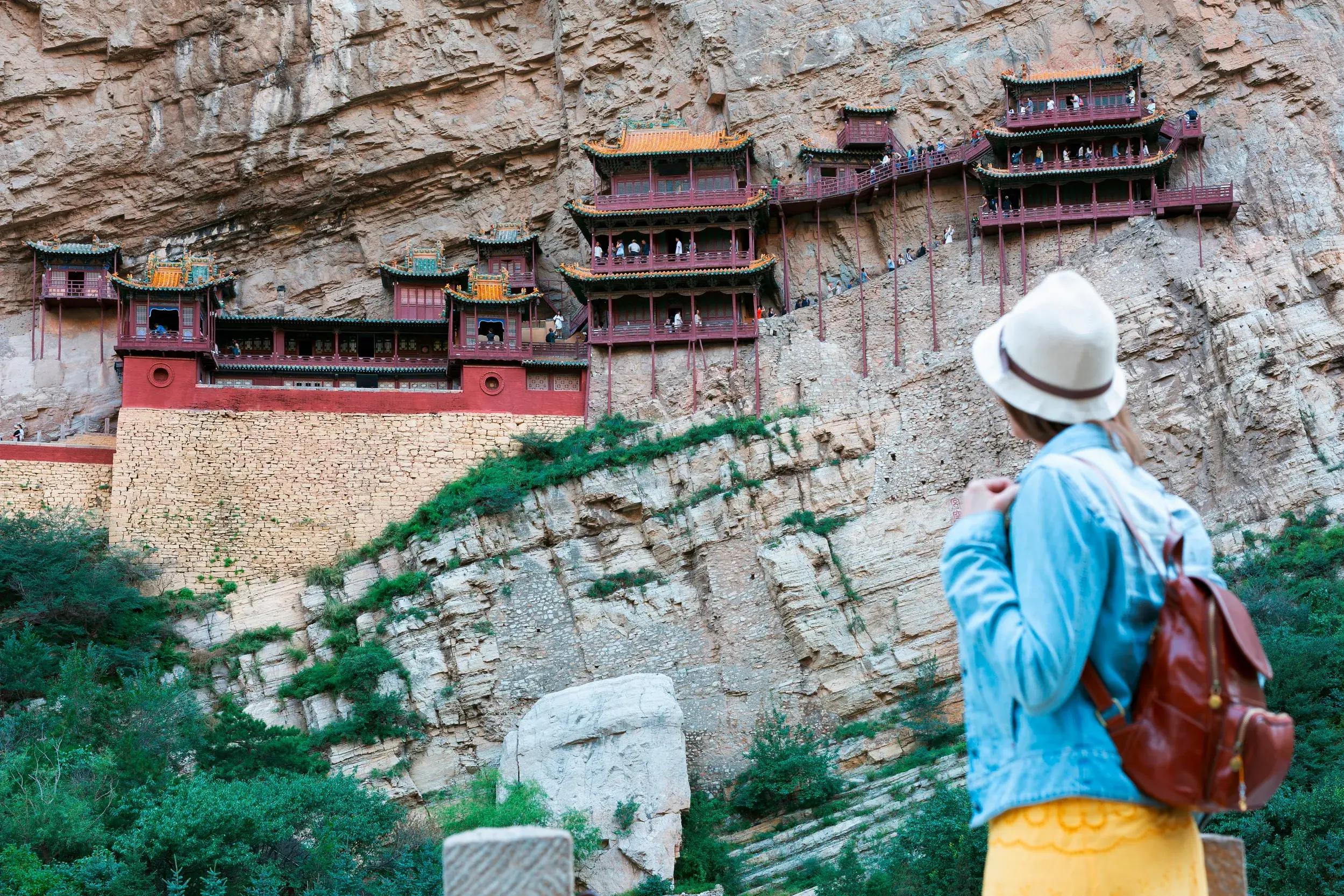 Junge Frau blickt auf das Hängende Kloster Xuankong Si, das spektakulär in eine Felswand in China gebaut ist.