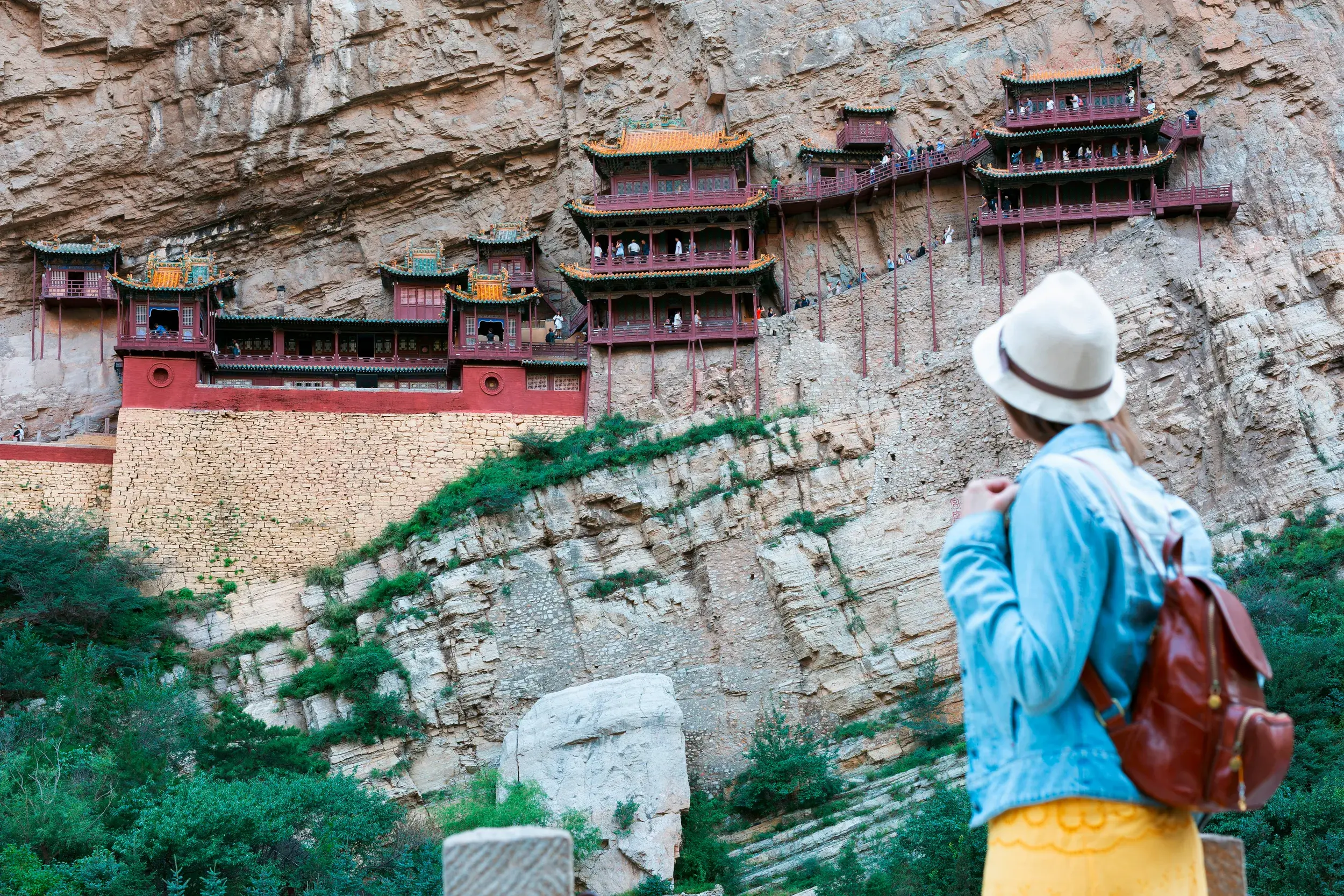 Junge Frau blickt auf das Hängende Kloster Xuankong Si, das spektakulär in eine Felswand in China gebaut ist.