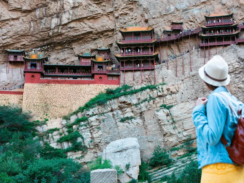 Junge Frau blickt auf das Hängende Kloster Xuankong Si, das spektakulär in eine Felswand in China gebaut ist.