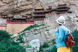 Junge Frau blickt auf das Hängende Kloster Xuankong Si, das spektakulär in eine Felswand in China gebaut ist.