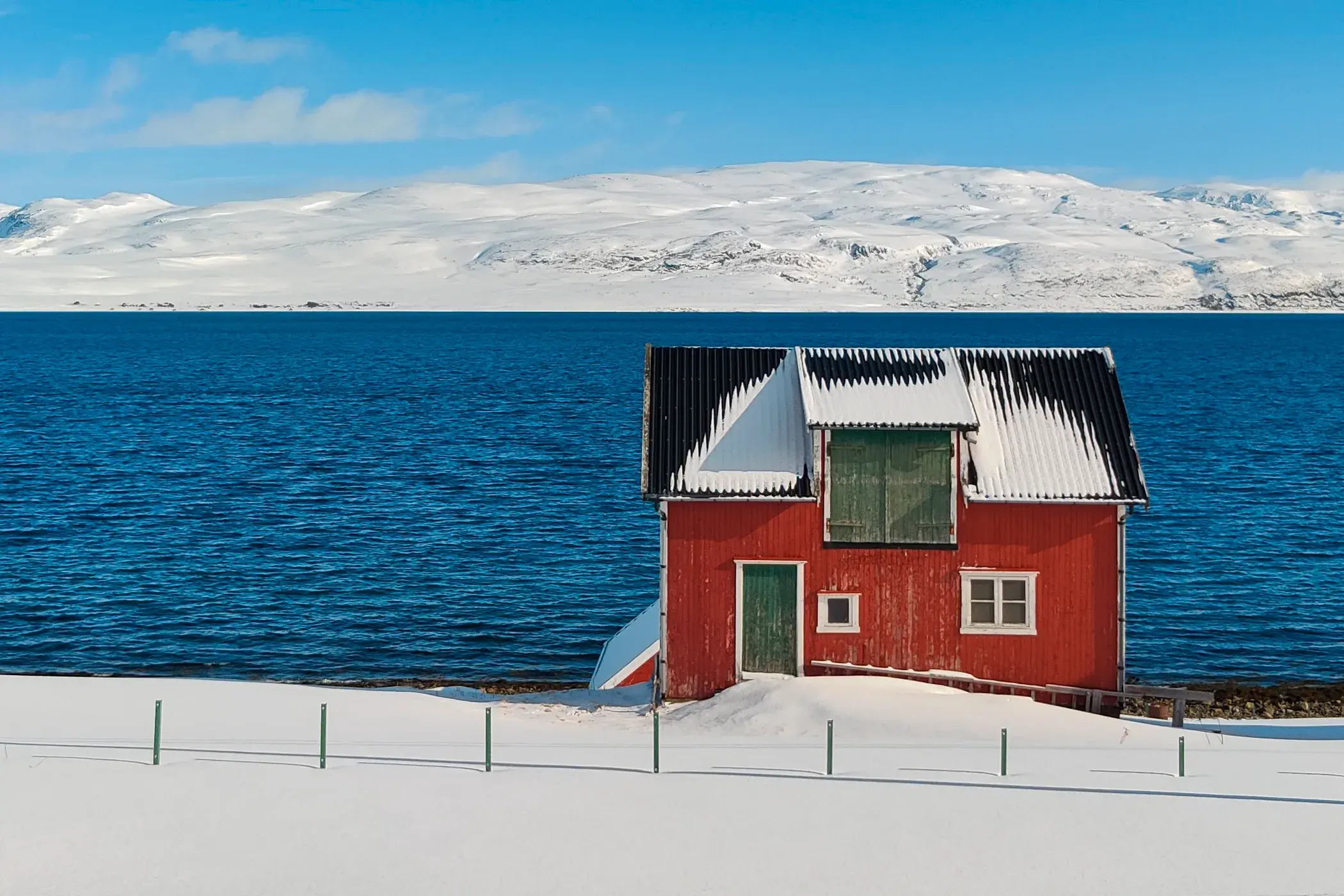 Eine typisch rote Fischerhütte in der verschneiten Fjordlandschaft Nordnorwegens unter einem strahlend blauen Winterhimmel.