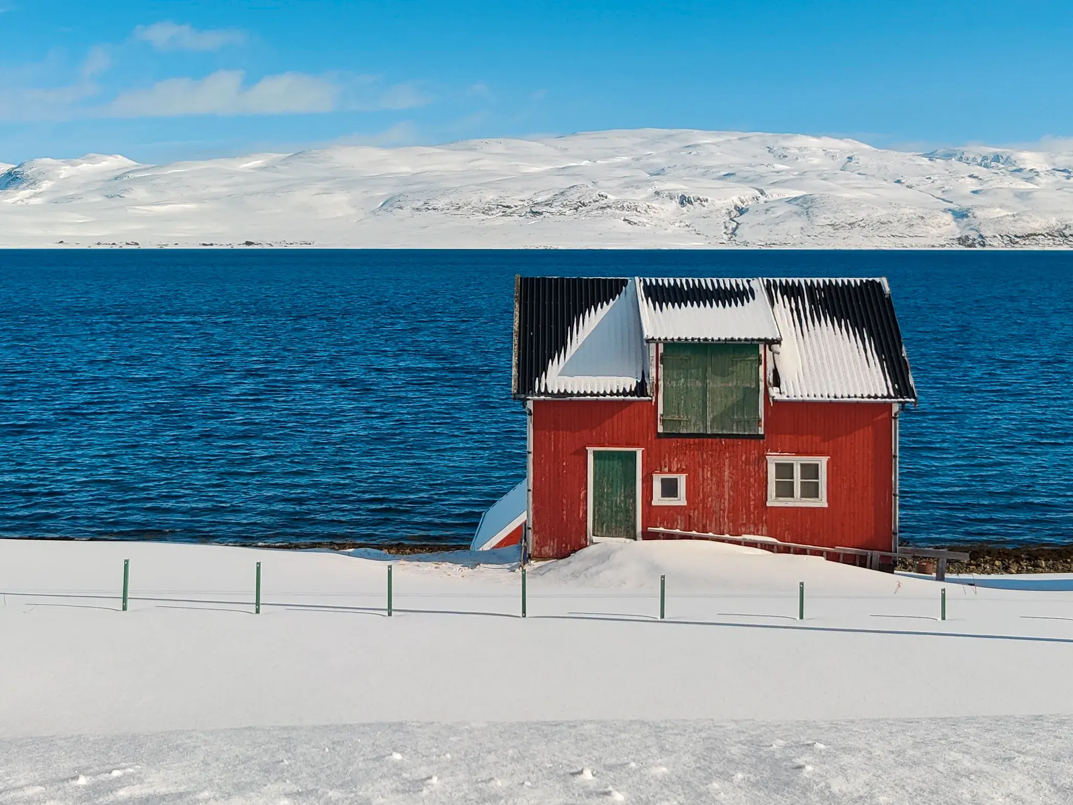Eine typisch rote Fischerhütte in der verschneiten Fjordlandschaft Nordnorwegens unter einem strahlend blauen Winterhimmel.