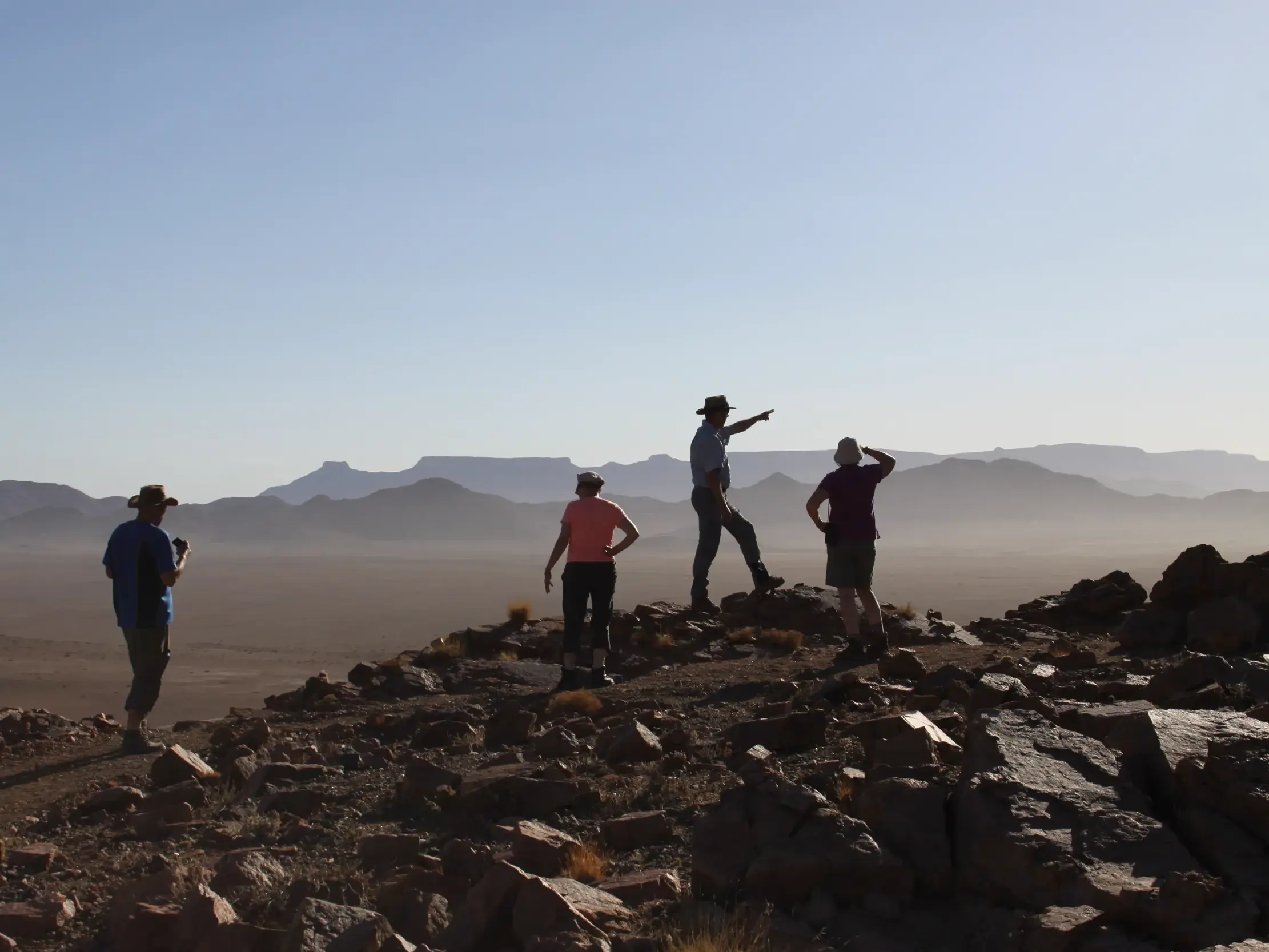 Eine vierköpfige Wandergruppe mit Reiseleiter genießt auf einem Felsen die Aussicht über die Berglandschaft im Erongo-Gebirge, Namibia.
