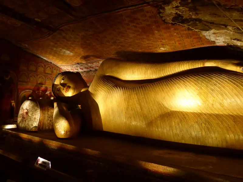 Große, goldene und liegende Buddha-Statue im Felsentempel von Dambulla, umgeben von alten, bunten Deckenmalereien.