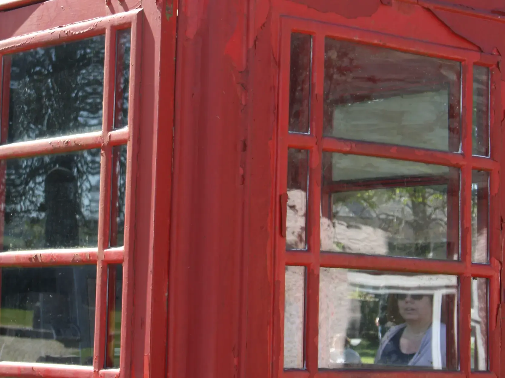 Eine Wanderin spiegelt sich im Fenster einer klassischen, roten Telefonzelle in einem Dorf in England auf dem Coast to Coast Walk.