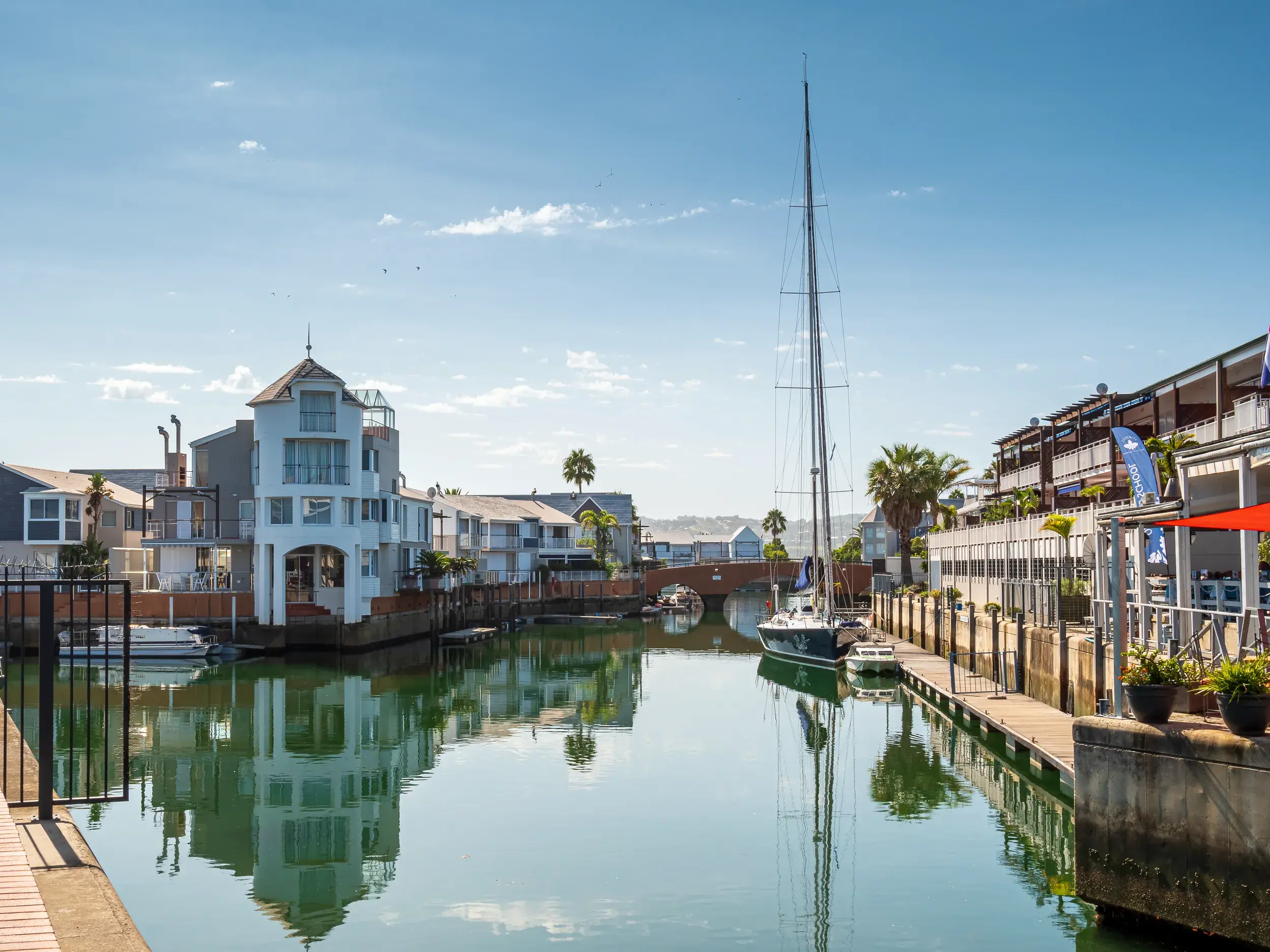 Ein Segelboot liegt im ruhigen Wasser der Knysna Waterfront vor malerischen Häusern an Südafrikas berühmter Gartenroute.