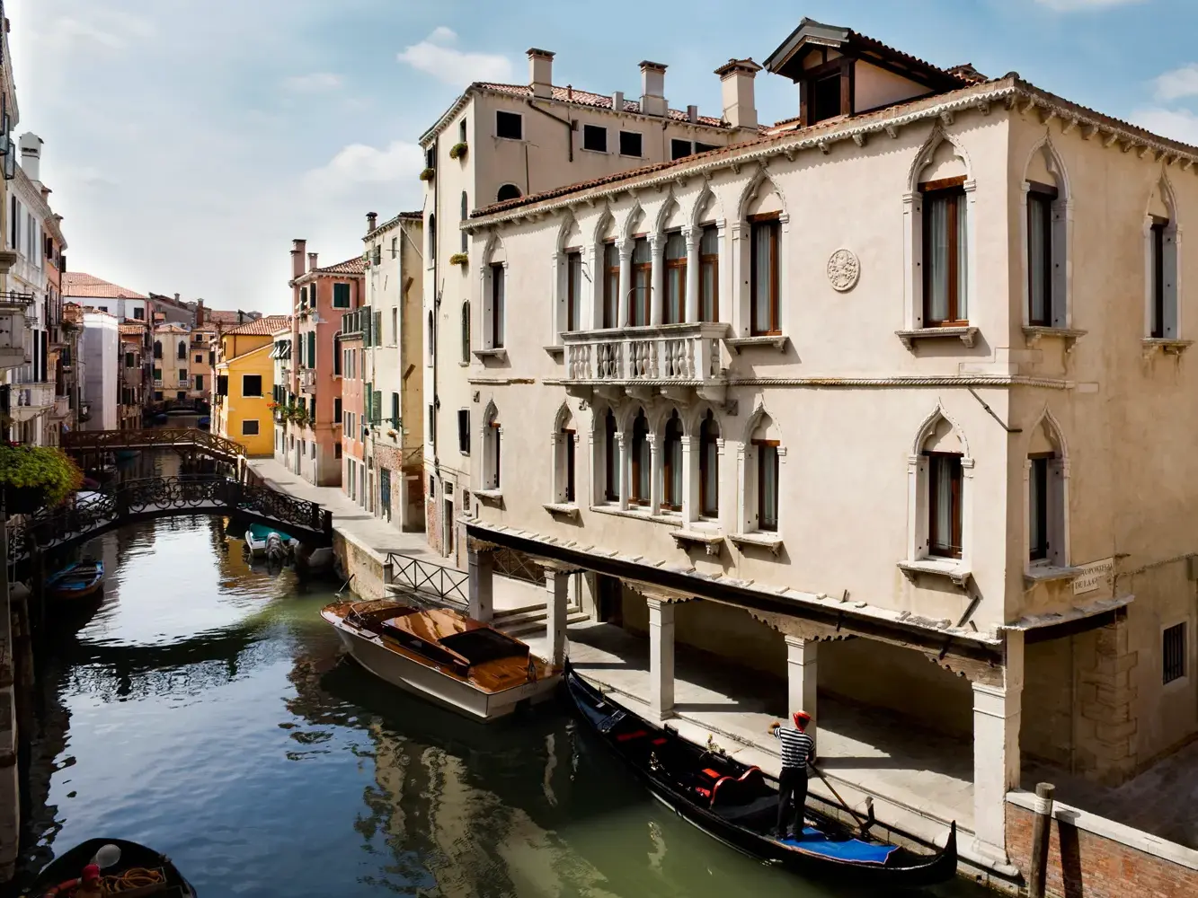 Historische Paläste an einem ruhigen Seitenkanal in Venedig, wo ein Gondoliere auf seiner Gondel unter einer Loggia wartet.