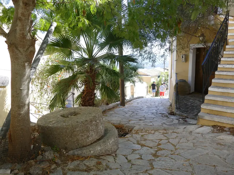 Historische Gasse mit Steinpflaster und einem alten Mühlstein in einem Bergdorf auf dem Korfu-Trail.