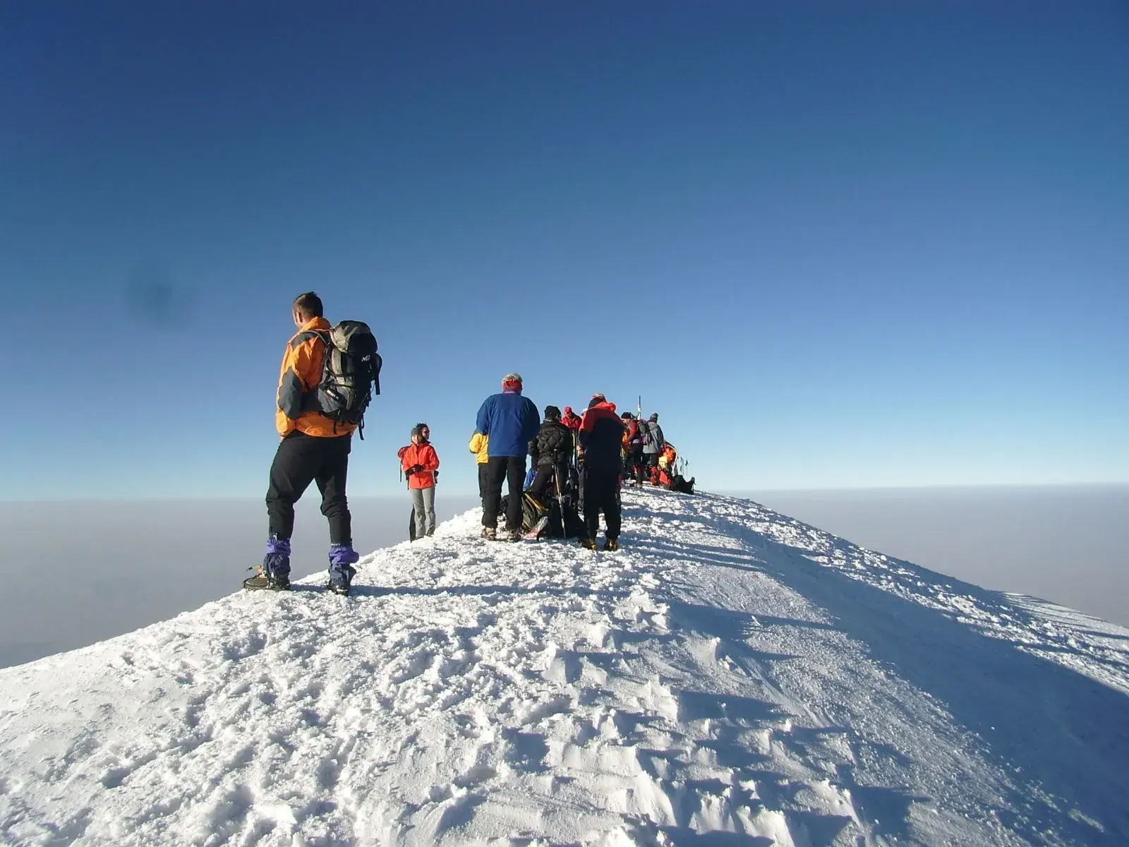 Eine Hauser-Trekkinggruppe steht nach der Gipfelbesteigung auf dem schneebedeckten Ararat und blickt über ein Wolkenmeer.