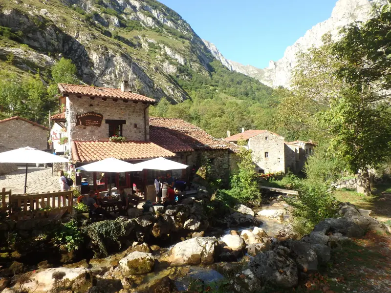 Wanderer machen eine Pause auf der Terrasse eines Steinhauses an einem Bach in den Bergen der Picos de Europa in Asturien.