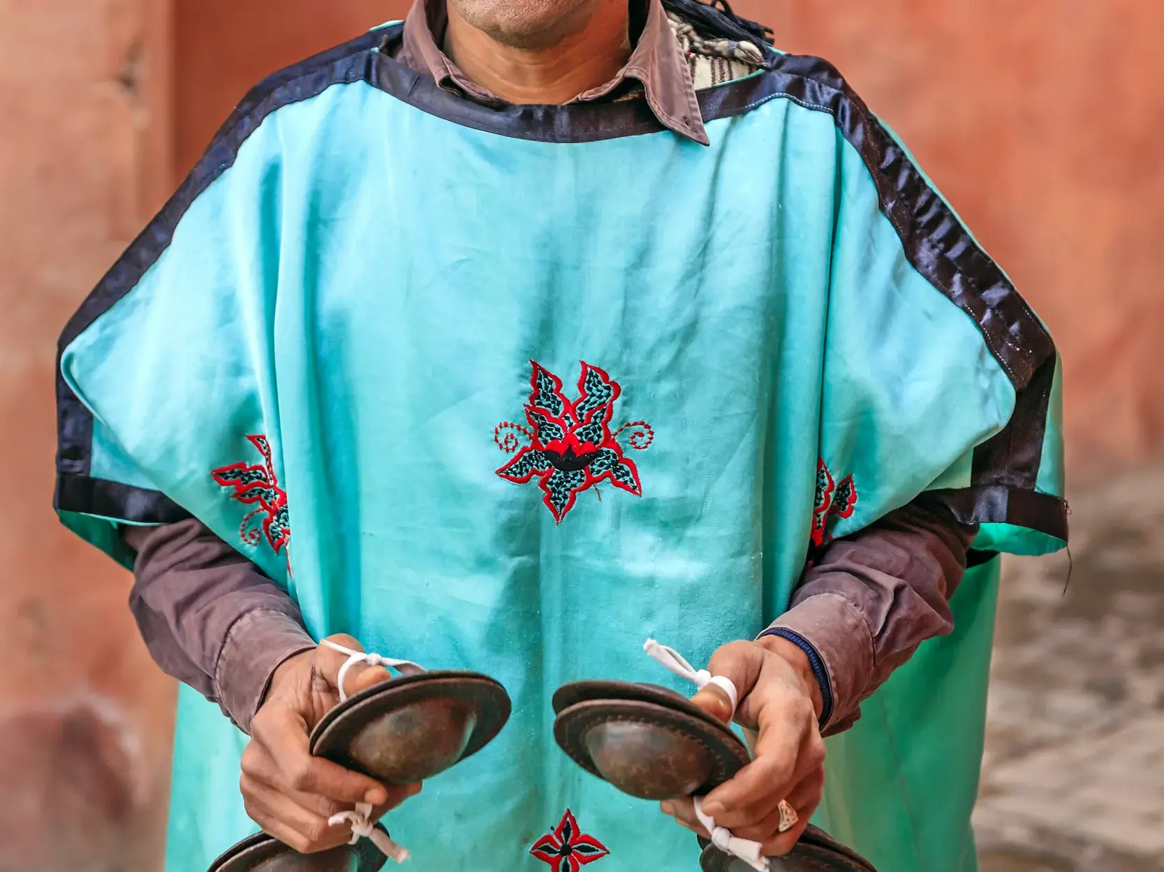 Nahaufnahme eines Gnawa-Musikers in blauer Tunika, der auf dem Djemaa el-Fna in Marrakesch mit Qraqeb-Kastagnetten musiziert.