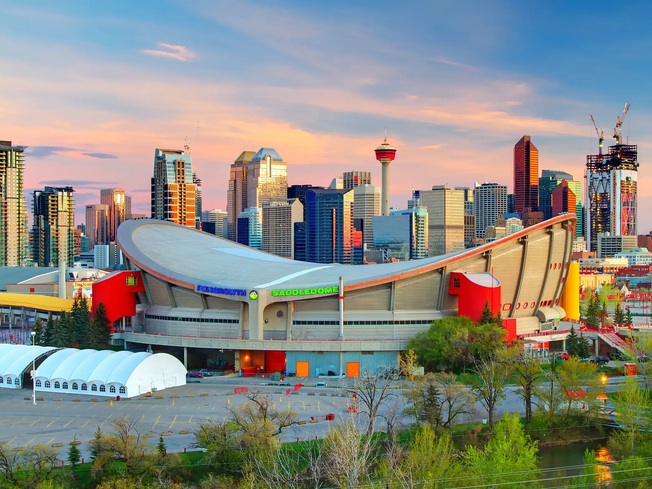 Der Scotiabank Saddledome vor der Skyline Calgarys mit dem Calgary Tower im warmen Licht des Sonnenuntergangs in Westkanada.