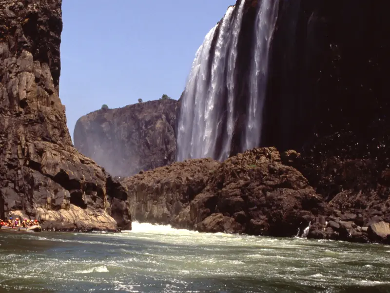 Eine Reisegruppe in einem Schlauchboot beim Rafting auf dem Sambesi am Fuße der mächtigen Victoriafälle in Simbabwe.