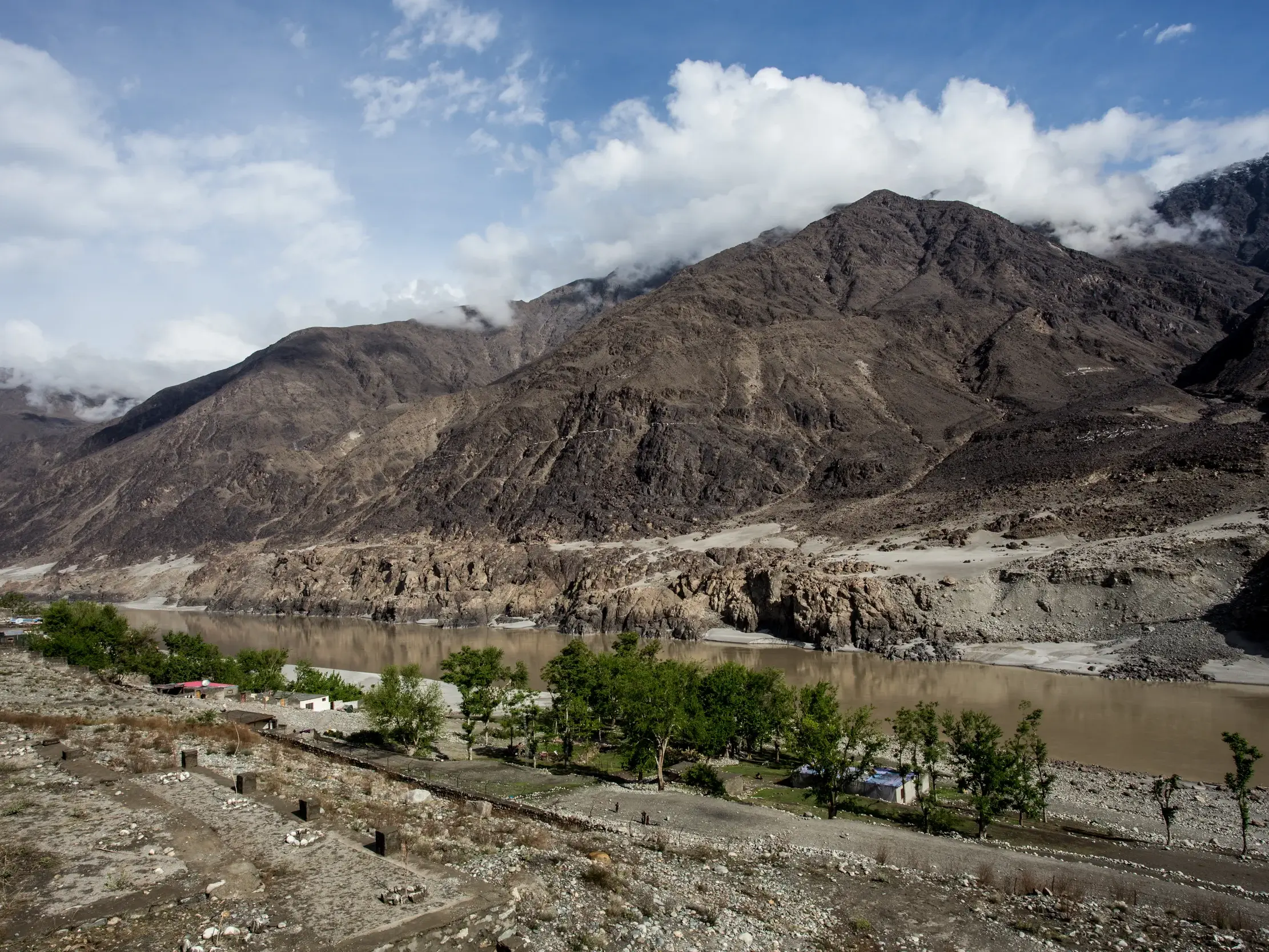 Weites, trockenes Flusstal in Pakistan mit Blick auf die wolkenverhangenen, kargen Berge des Karakorum-Gebirges.