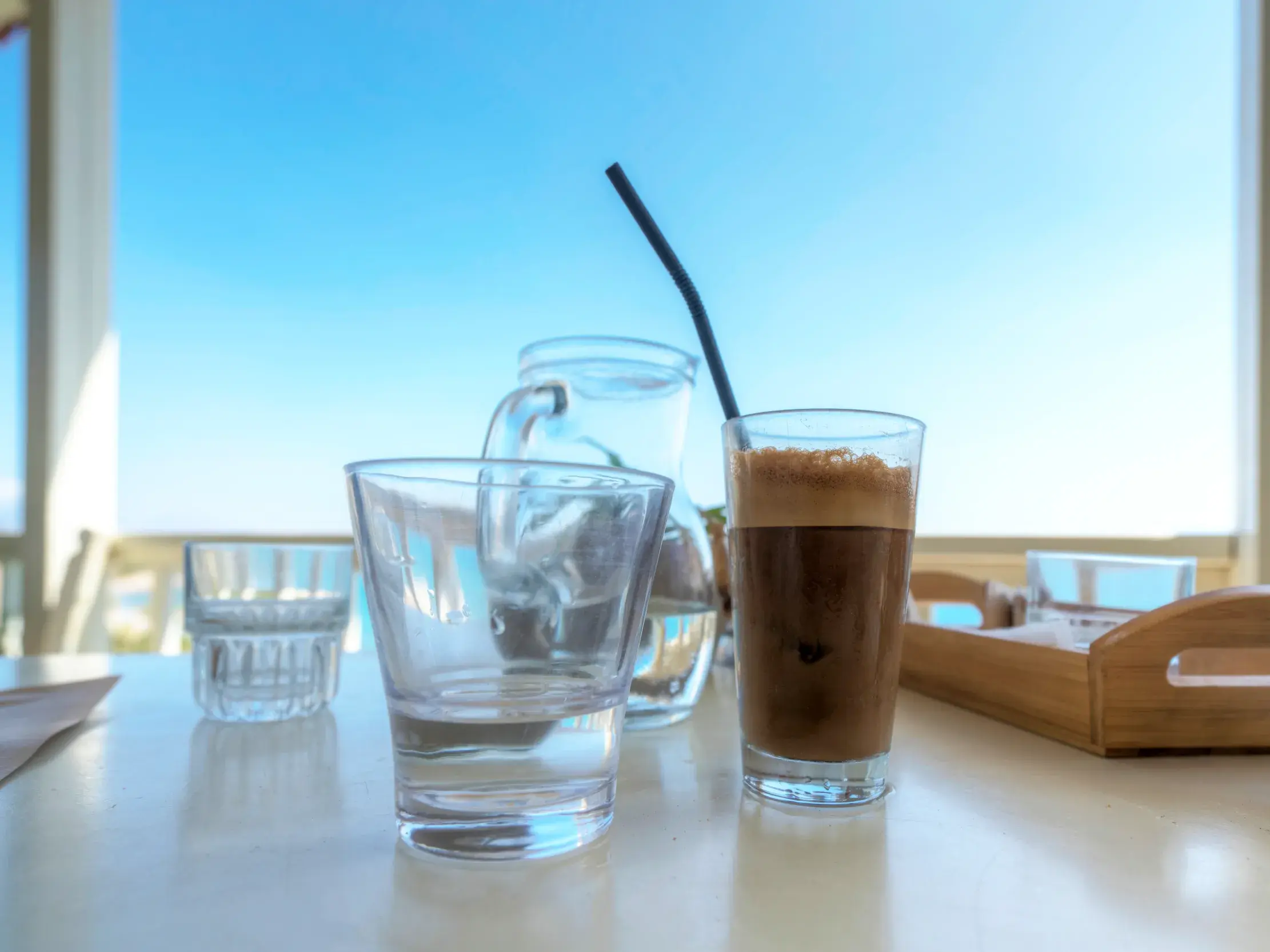Moment der Muße auf Kreta: ein griechischer Frappé auf dem Tisch eines Cafés in Elounda mit Blick auf das blaue Meer.