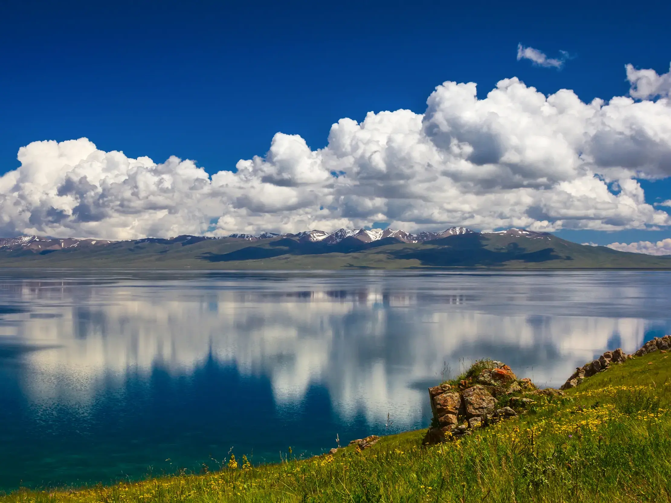 Malerischer Ausblick auf den Songköl See in Kirgistan, dessen spiegelglatte Oberfläche Wolken und die Tian-Shan-Berge reflektiert.