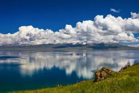Malerischer Ausblick auf den Songköl See in Kirgistan, dessen spiegelglatte Oberfläche Wolken und die Tian-Shan-Berge reflektiert.