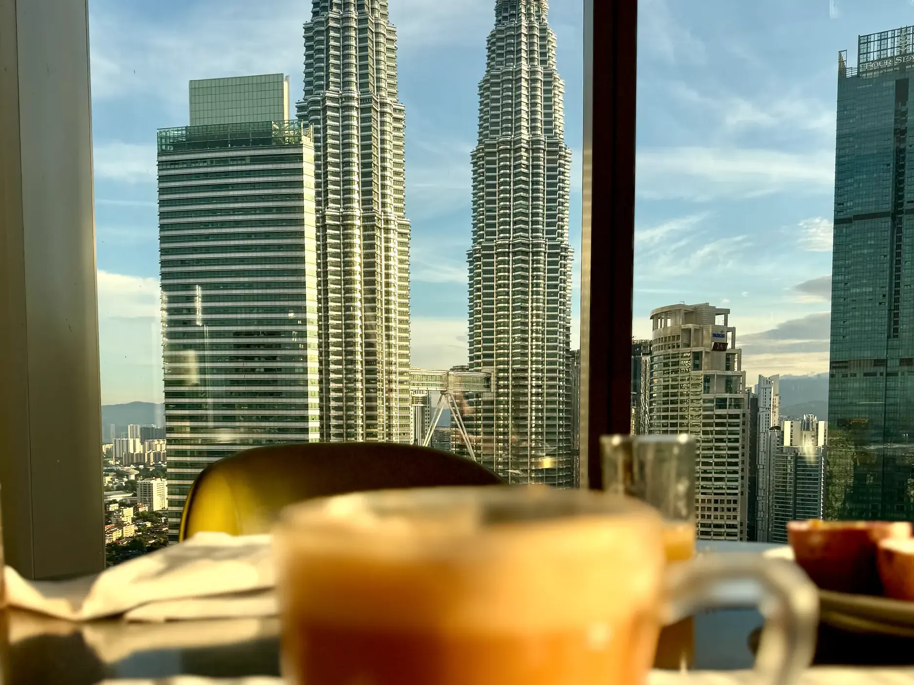 Blick aus einem Hotelzimmer in Kuala Lumpur auf die berühmten Petronas Towers und die Skyline der Stadt im warmen Morgenlicht.