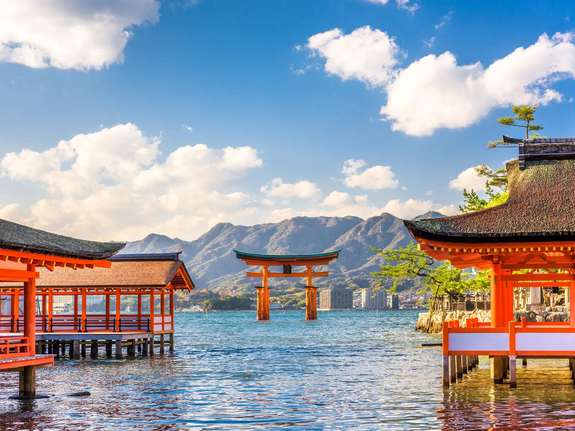 Rote Schreingebäude und das berühmte Torii des Itsukushima-Schreins im Wasser vor der Bergkulisse der Insel Miyajima.
