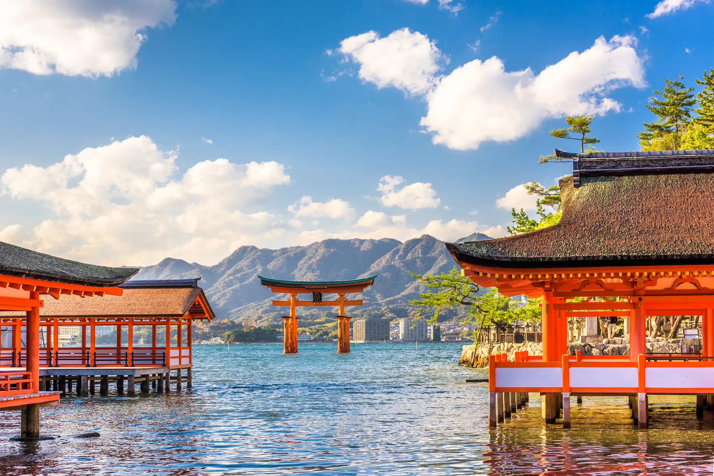 Rote Schreingebäude und das berühmte Torii des Itsukushima-Schreins im Wasser vor der Bergkulisse der Insel Miyajima.
