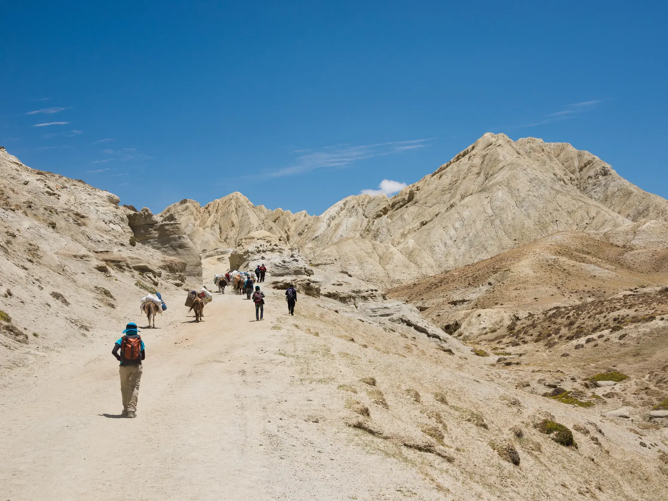 Eine Wandergruppe mit Begleitmannschaft und Packtieren auf einem Trekkingpfad in der kargen Felslandschaft von Mustang, Nepal.
