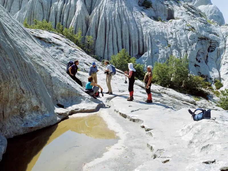 Eine kleine Wandergruppe macht eine Pause an einem Wasserloch inmitten der bizarren Kalksteinfelsen im Paklenica Nationalpark.
