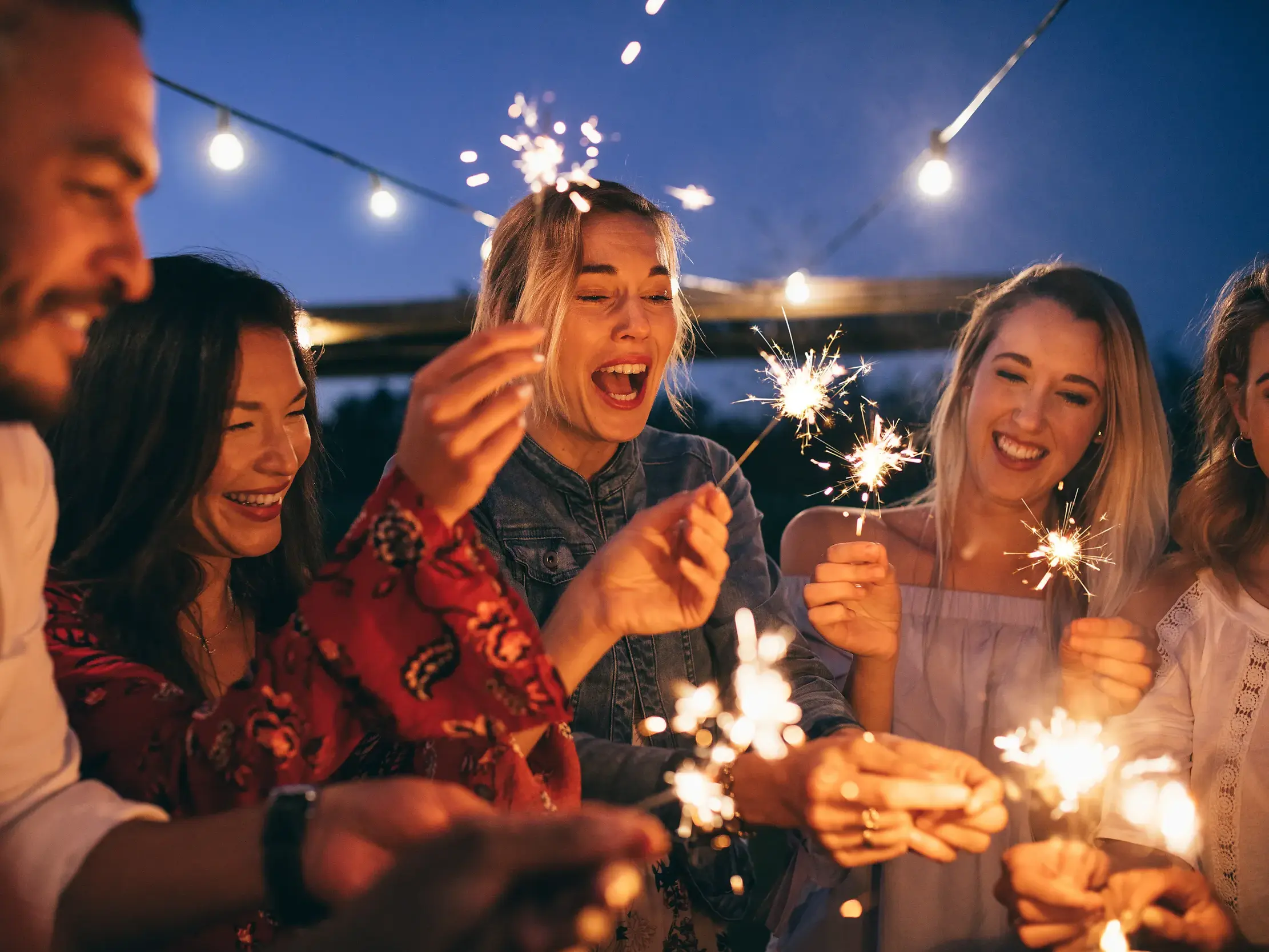Fröhliche Gruppe feiert bei einer Singlereise in Malta ausgelassen Silvester mit Wunderkerzen unter freiem Himmel.