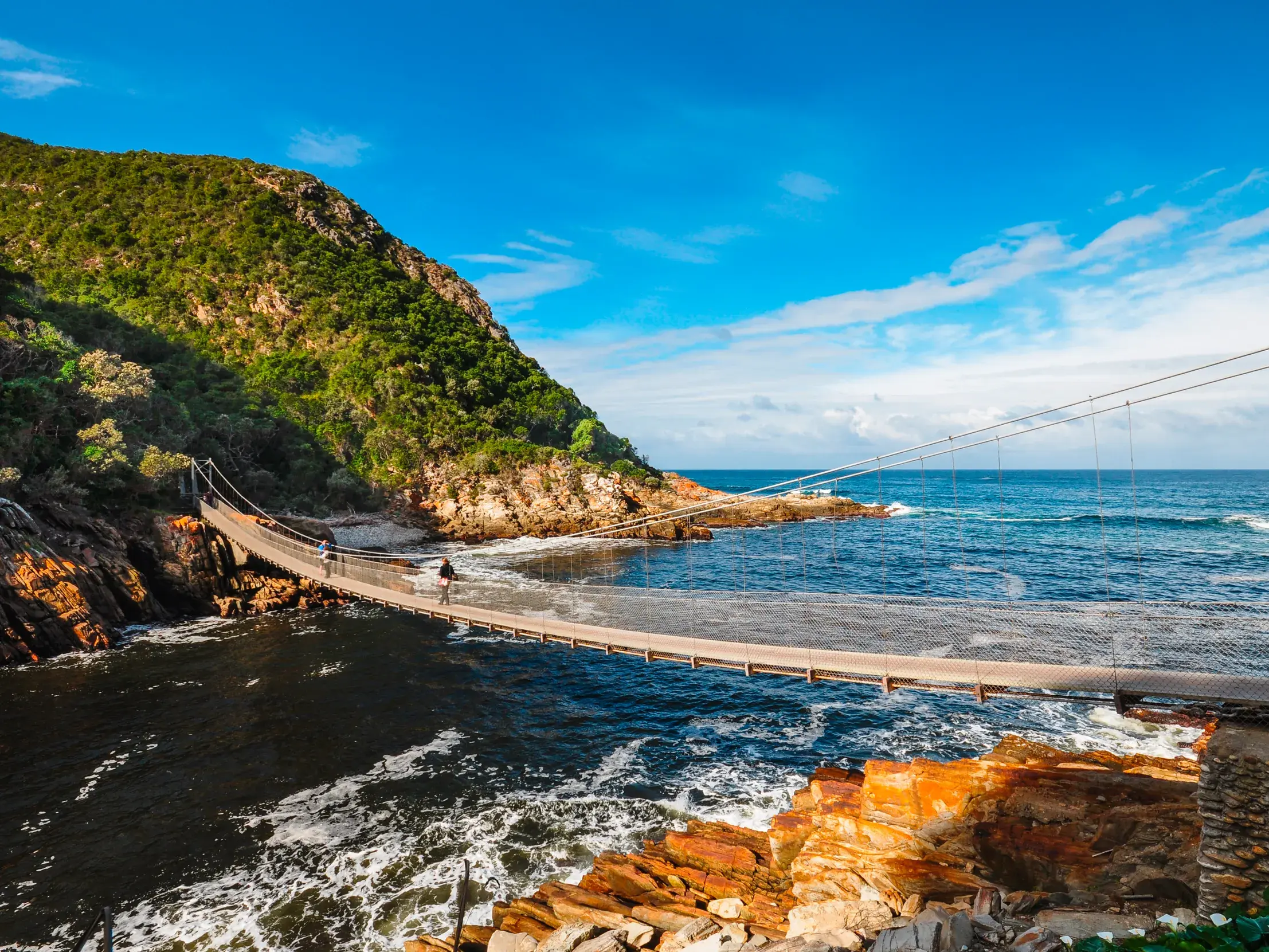 Reisende auf einer geführten Rundreise überqueren die lange Hängebrücke an der Storms River Mündung in Südafrika.