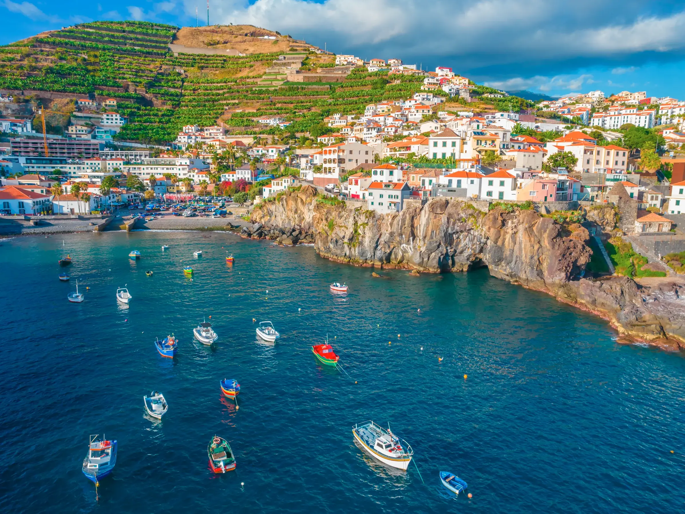 Luftaufnahme der malerischen Bucht von Câmara de Lobos auf Madeira mit bunten Fischerbooten im tiefblauen Atlantik.